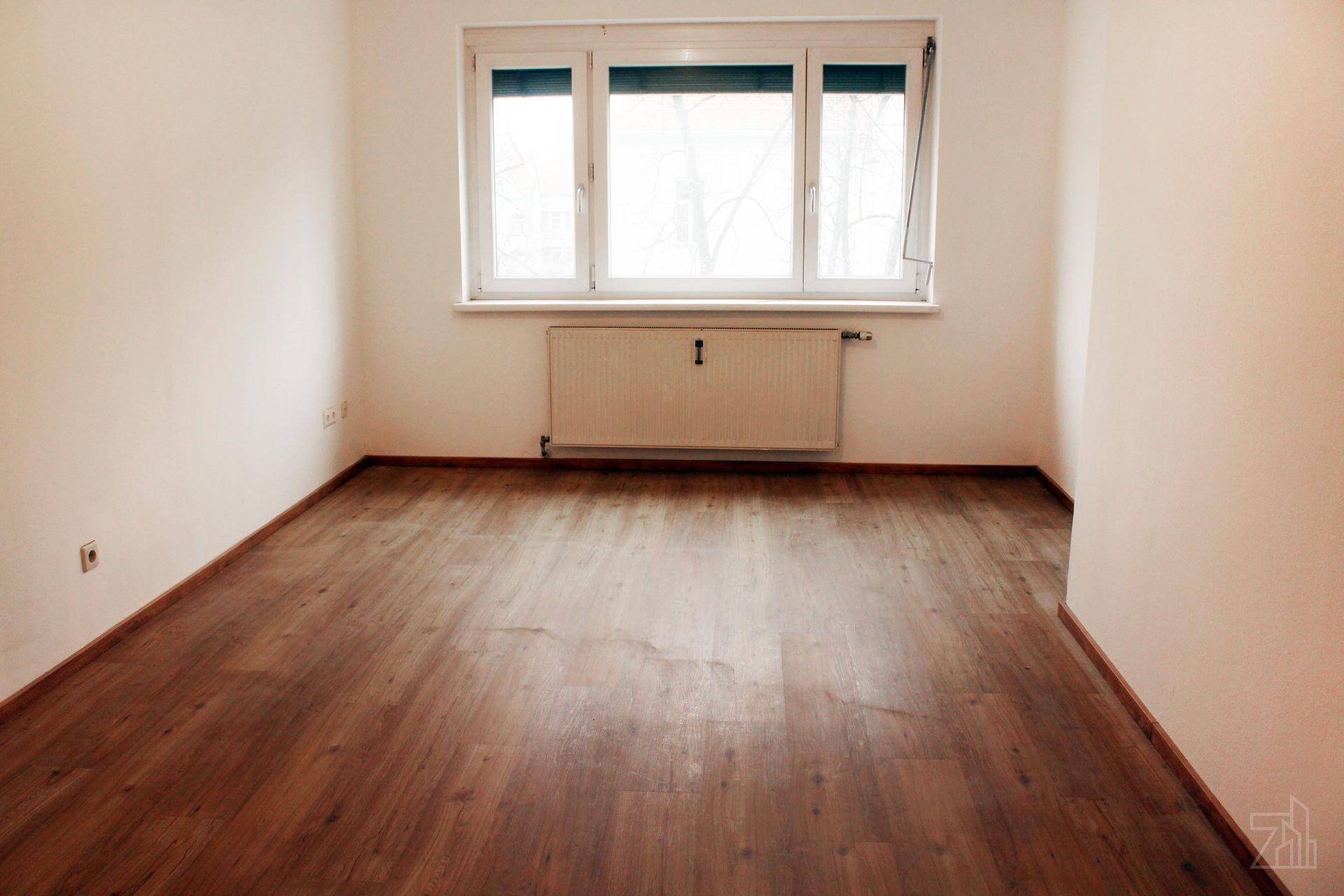 Leerer Raum mit Laminatboden, weißen Wänden und einem großen Fenster.