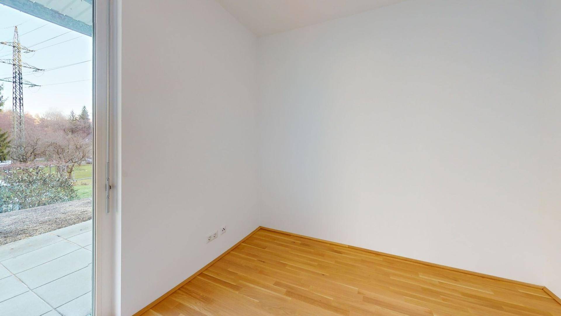 Heller, leerer Raum mit Holzboden und Zugang zu einem Außenbereich mit Weitblick.