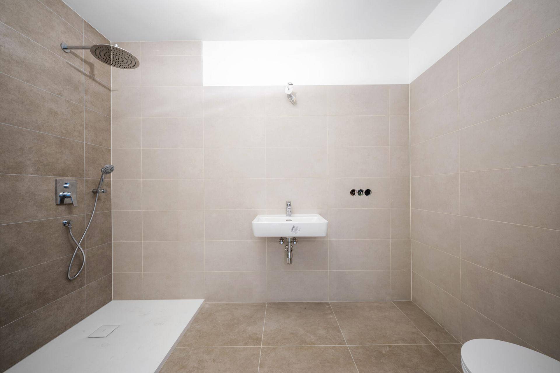 Modernes Badezimmer mit beigefarbenen Fliesen, einer ebenerdigen Dusche und einem Wandwaschbecken.