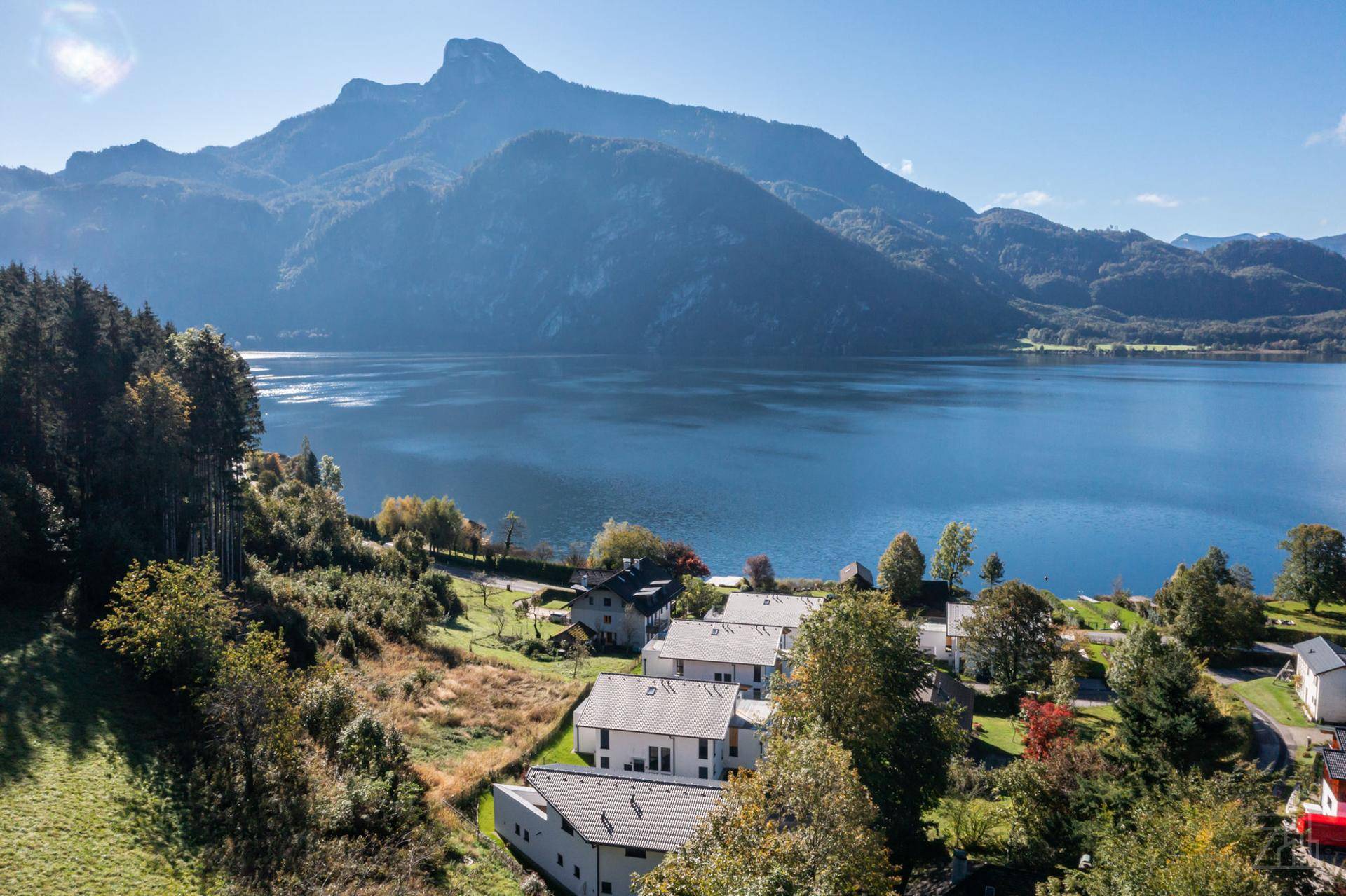 Panoramablick auf moderne Häuser am Seeufer mit majestätischen Bergen im Hintergrund.