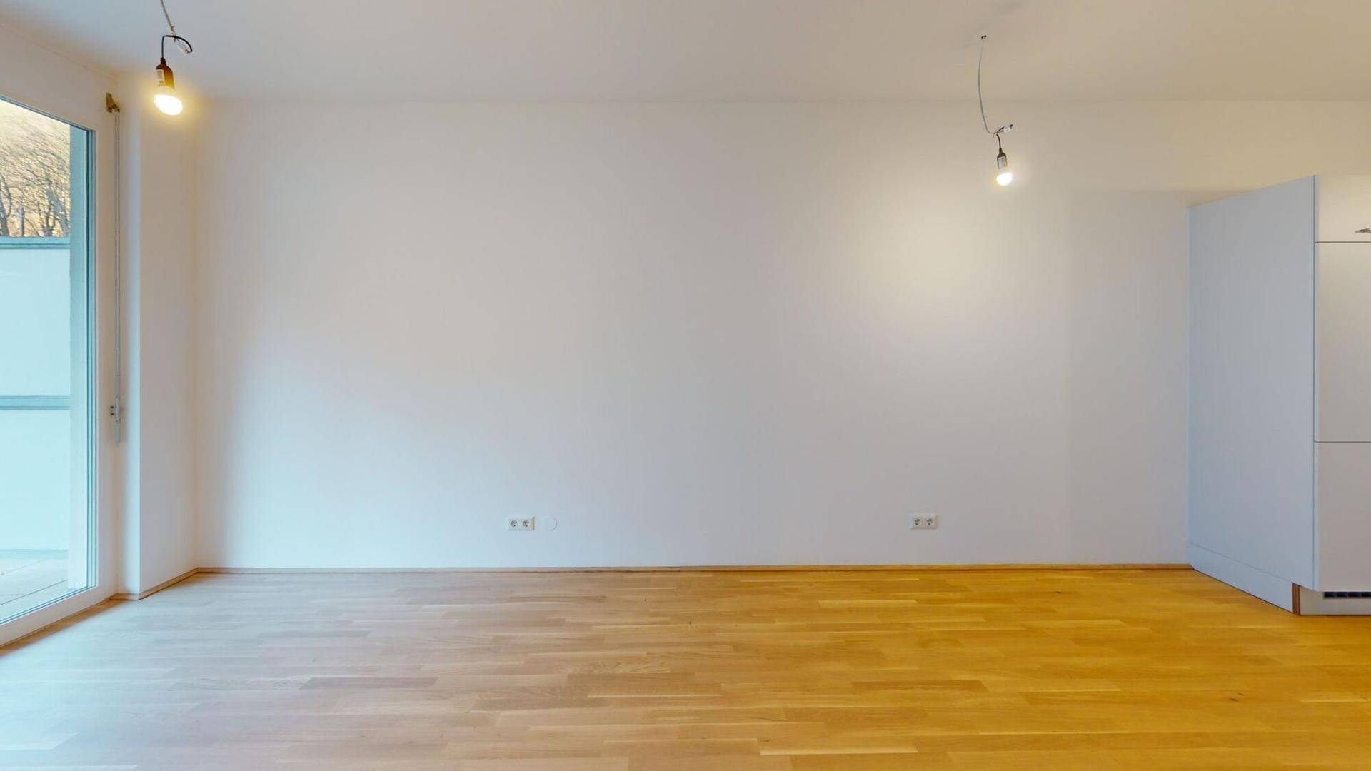 Heller, leerer Wohnraum mit Parkettboden und Zugang zu einem Außenbereich.