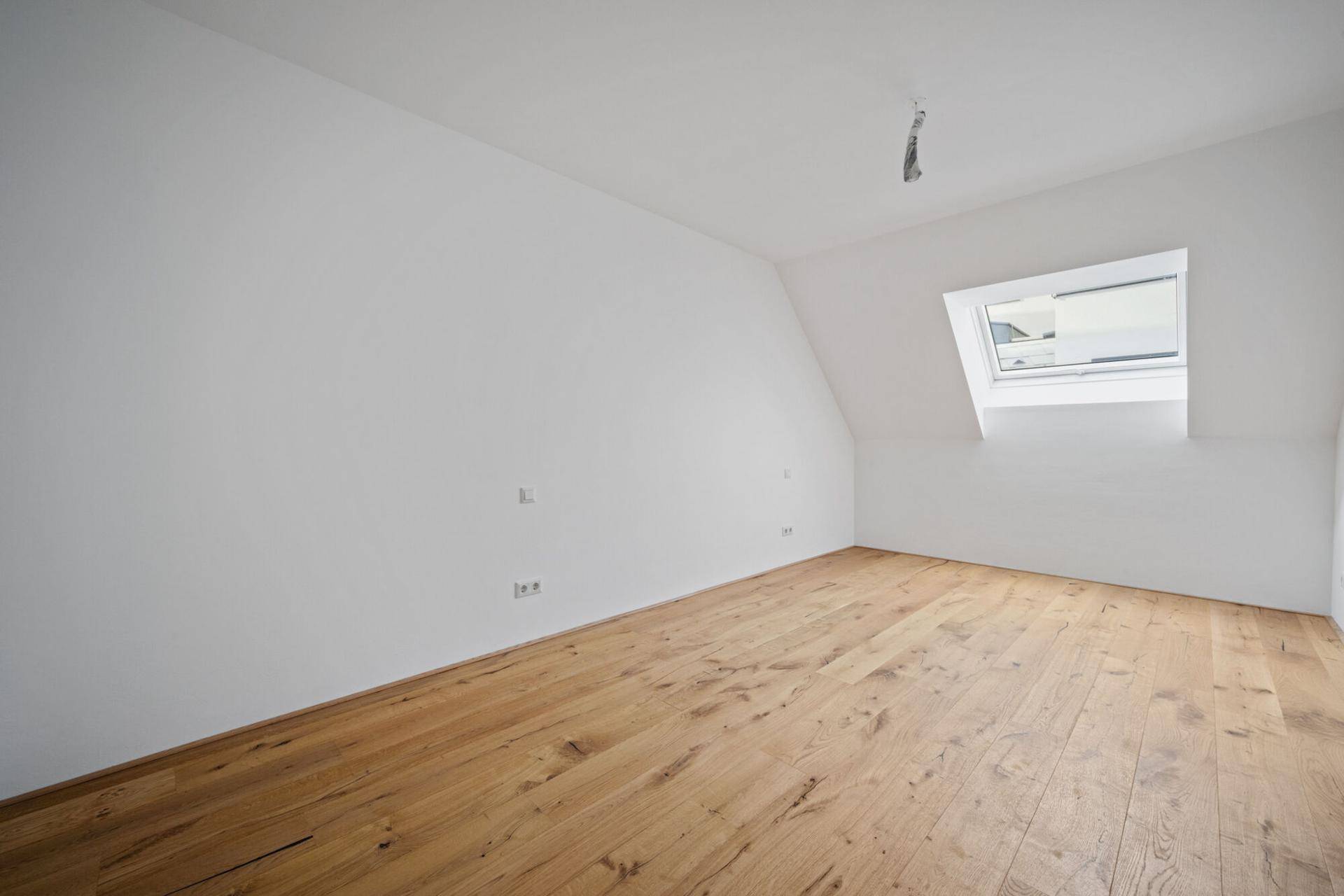 Geräumiges Zimmer mit Holzboden, Dachschräge und einem Dachfenster für natürliches Licht.