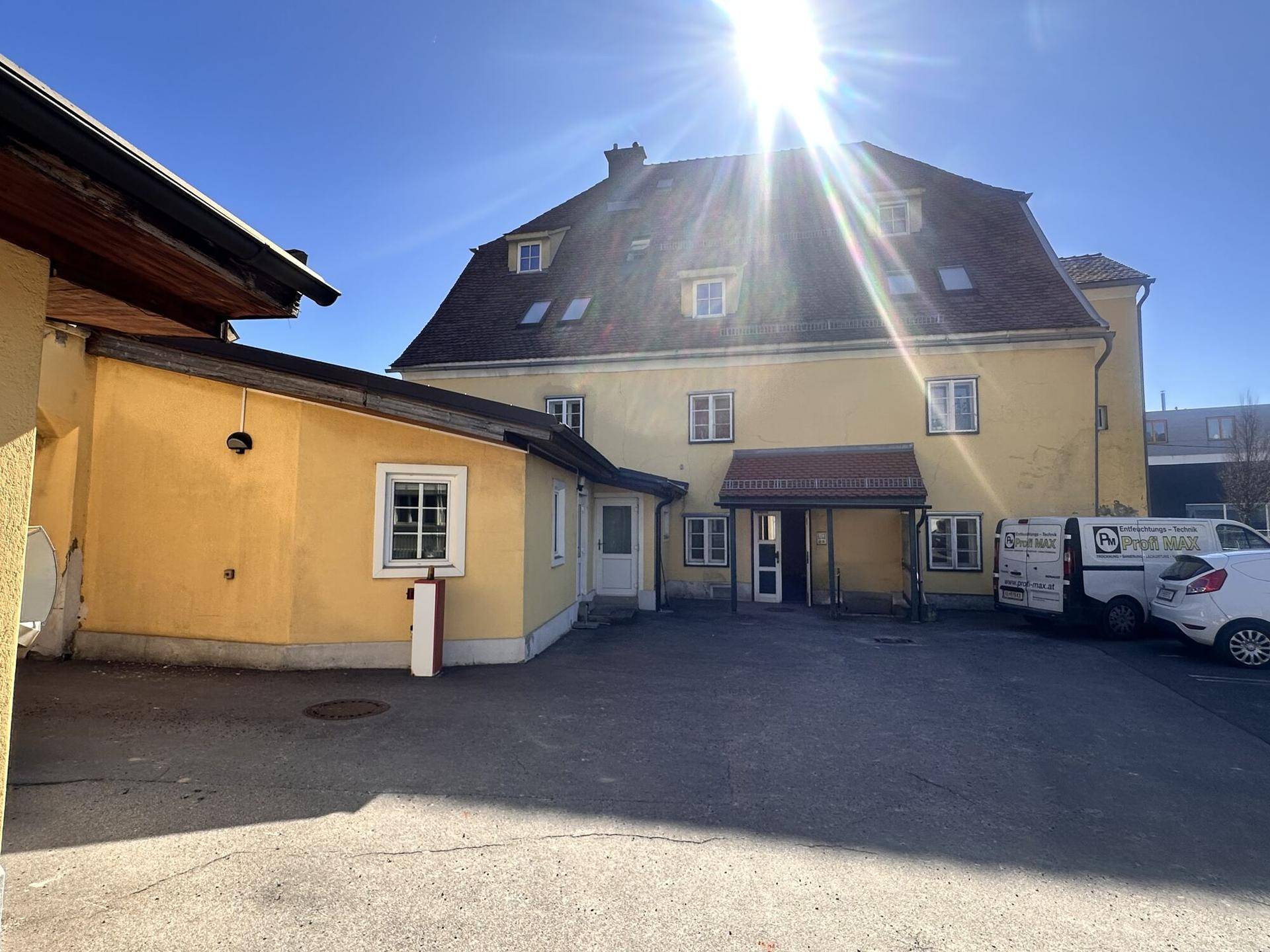Rückansicht des Gebäudes mit Parkplatz und sonnigem Himmel.