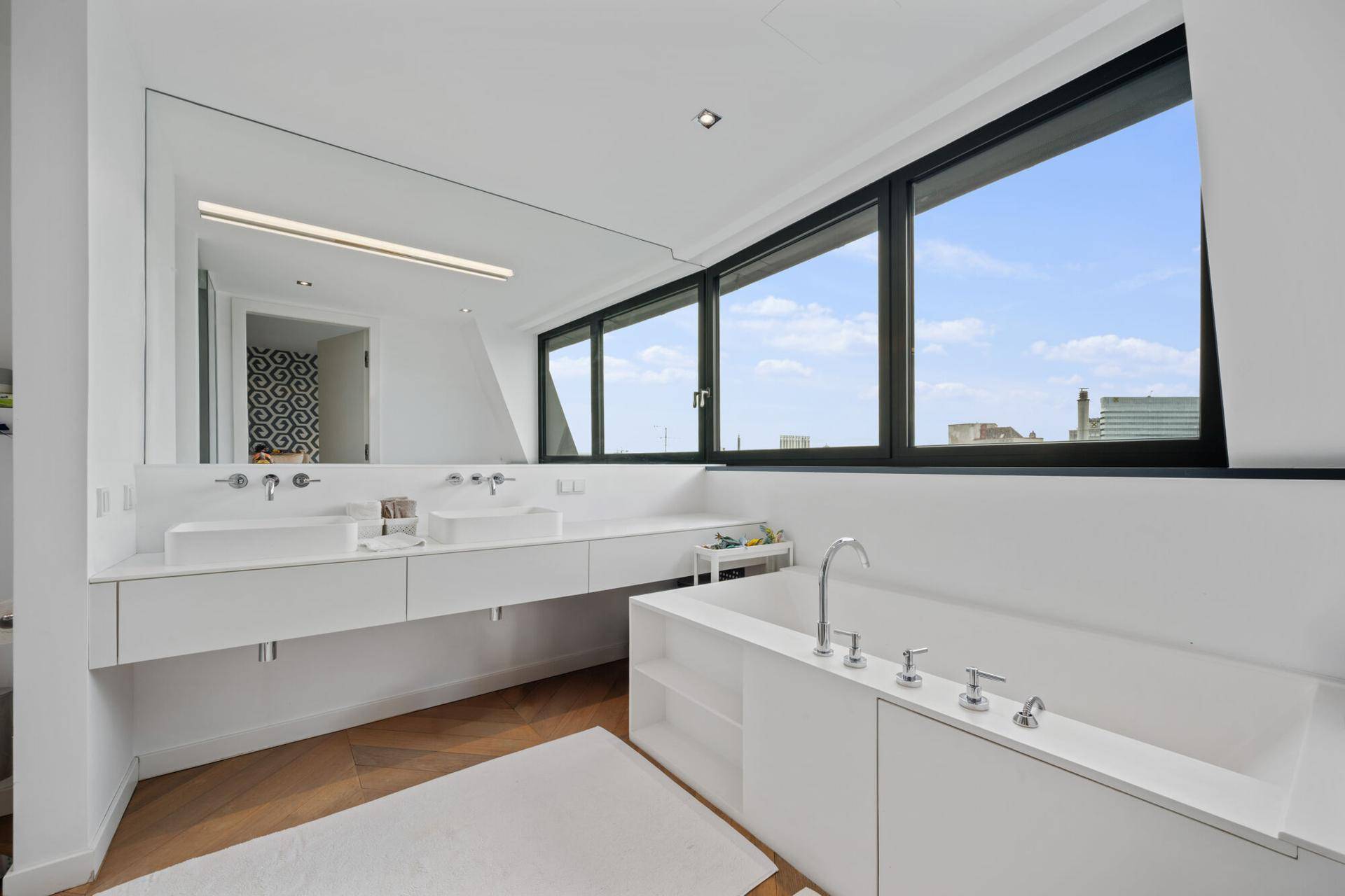 Helles Badezimmer mit Doppelwaschbecken, Badewanne und großen Fenstern mit Stadtblick.