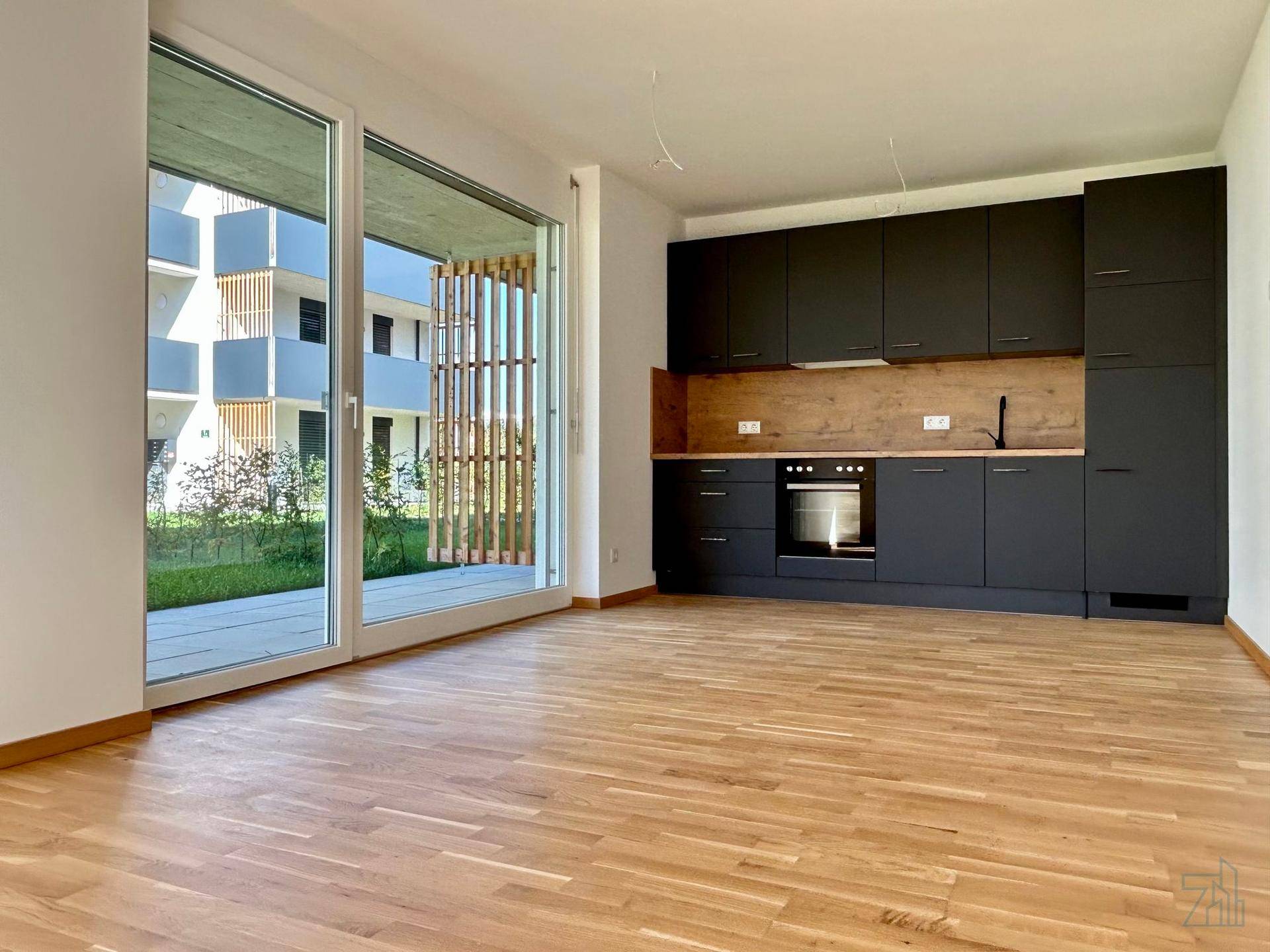 Heller Wohn-Essbereich mit moderner schwarzer Einbauküche, Holzarbeitsplatte und Zugang zur Terrasse.
