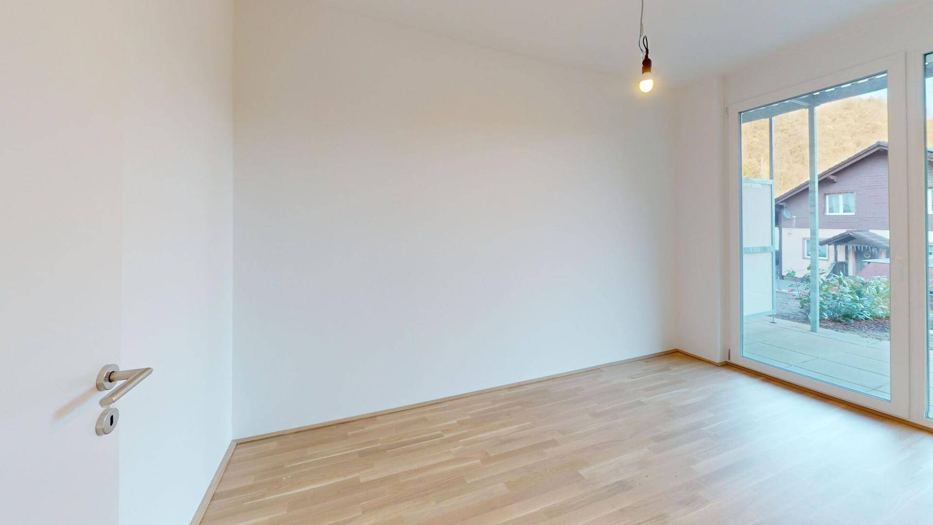 Heller, unmöblierter Raum mit Holzboden und großen Fenstern mit Blick auf die Umgebung.