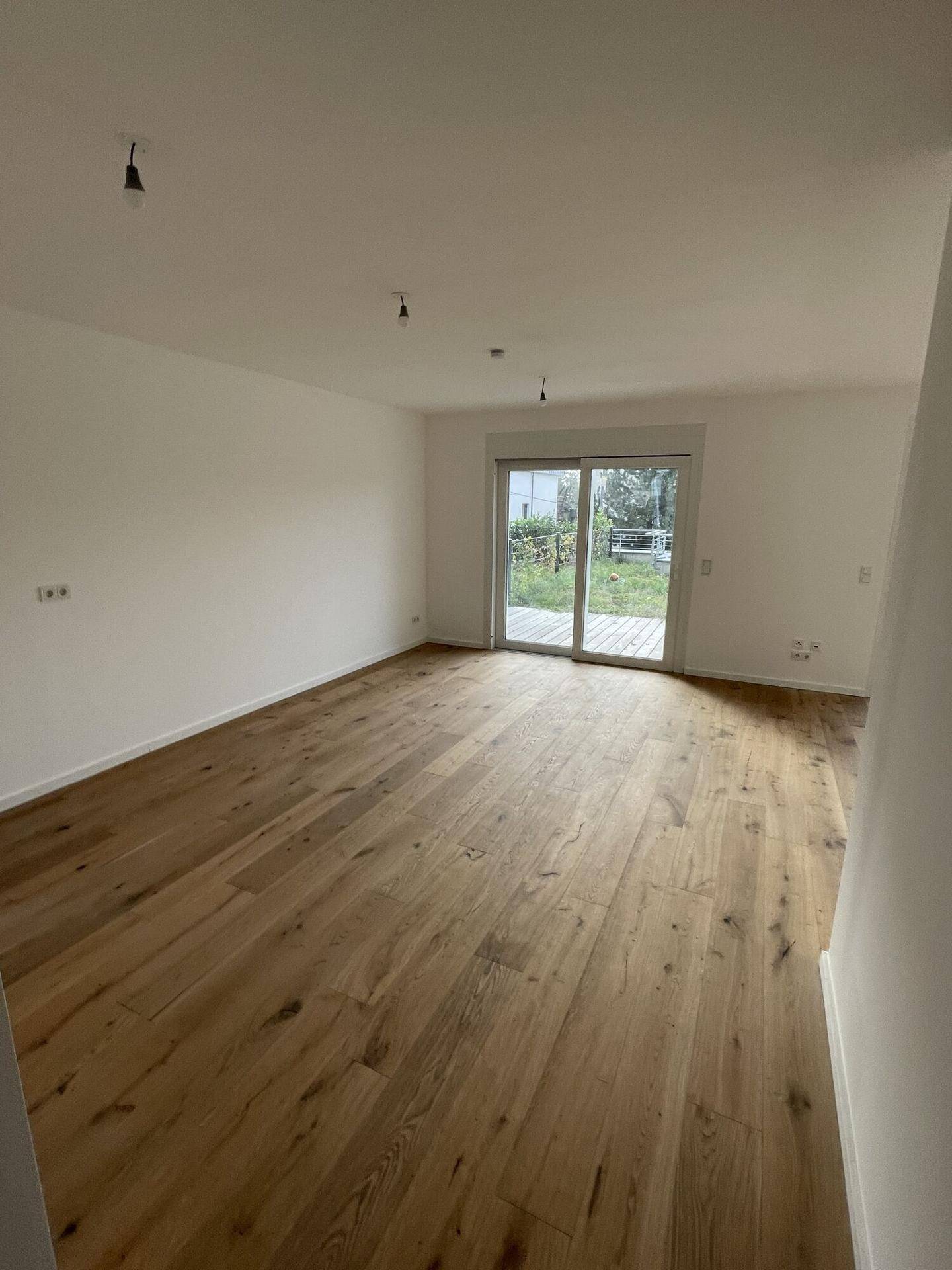Geräumiger Wohnbereich mit hellem Holzparkettboden und großer Schiebetür zum Außenbereich.