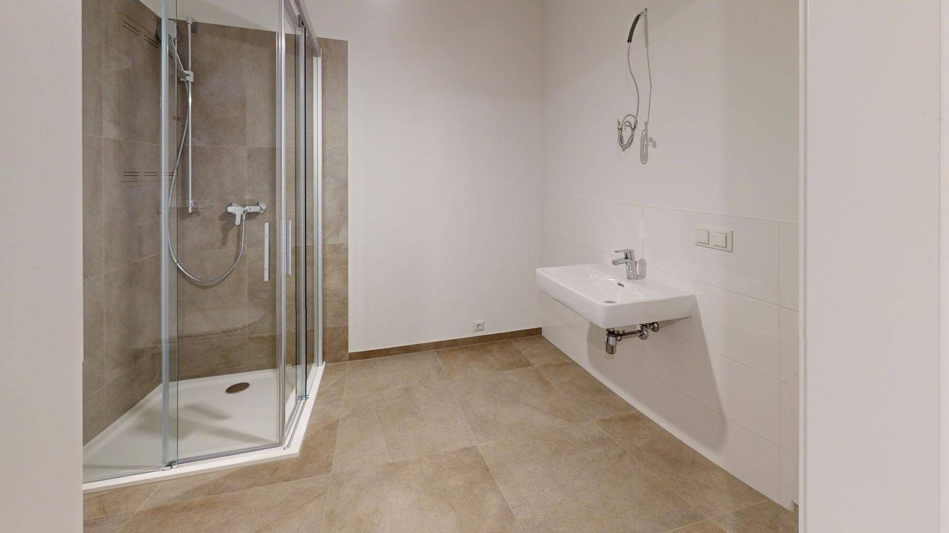 Modernes Badezimmer mit Duschkabine, wandhängendem Waschbecken und beigefarbenen Fliesen.