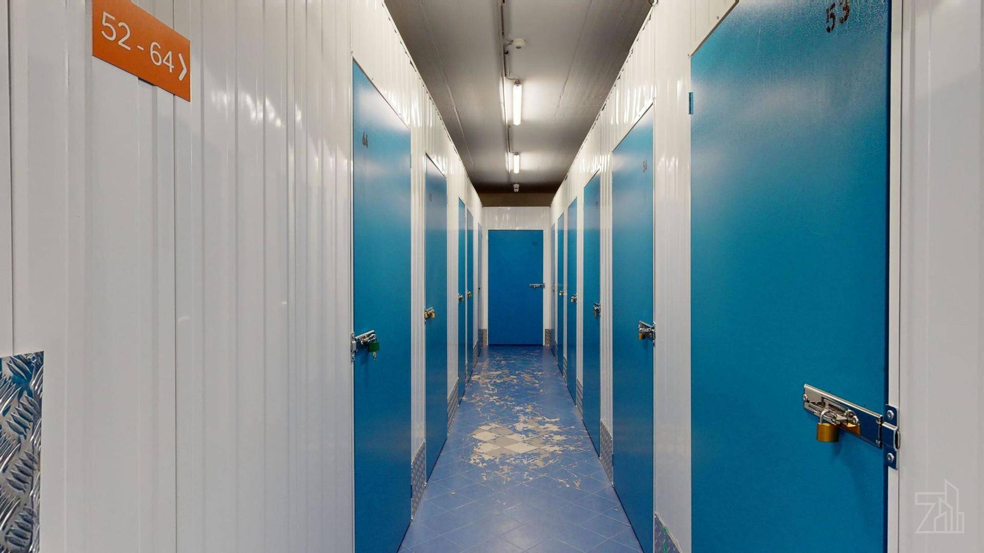 Gang in einem Lagerbereich mit nummerierten blauen Türen und weißen Wänden, gut beleuchtet.