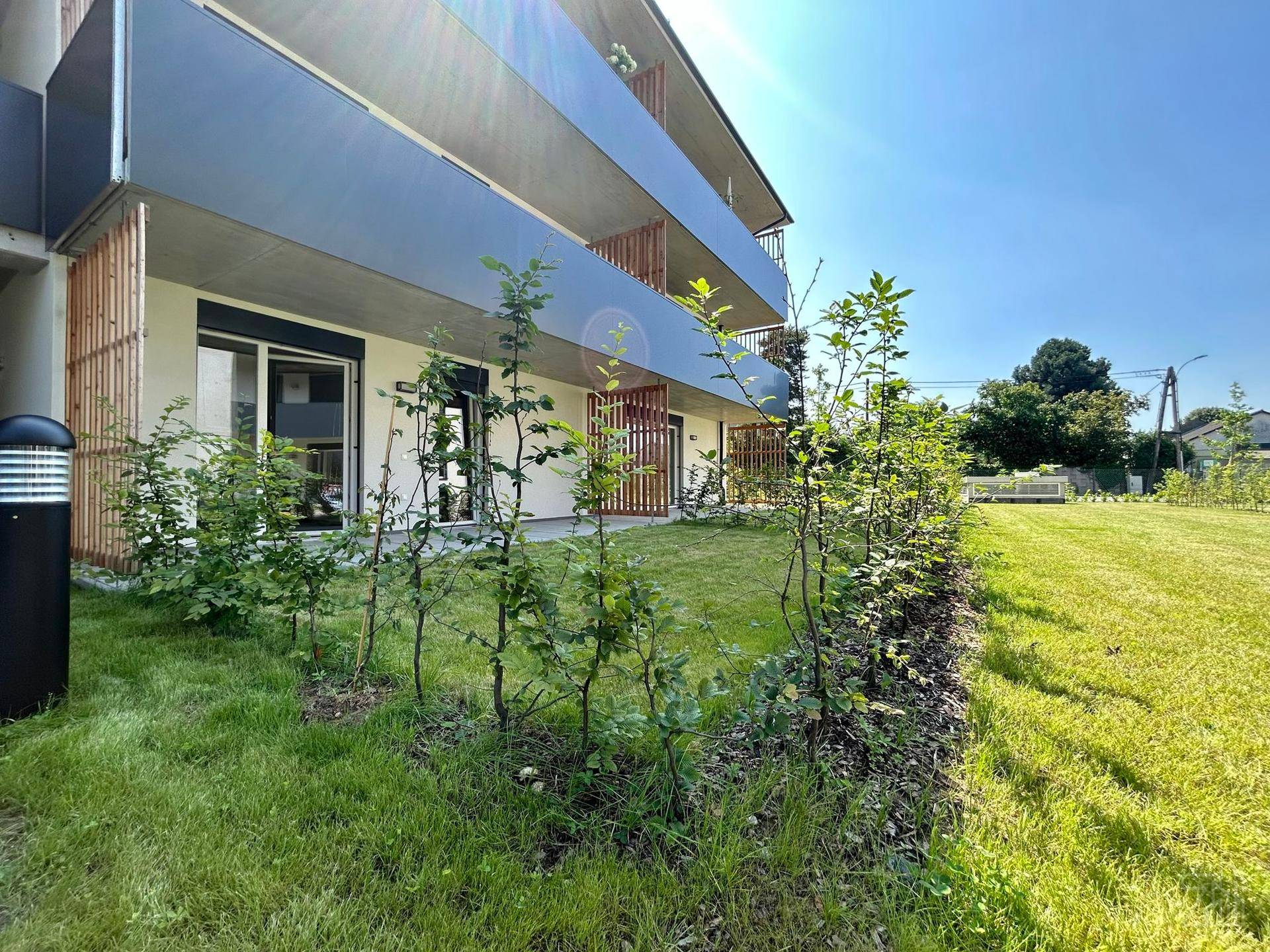 Modernes Apartmentgebäude mit Balkonen, umgeben von gepflegtem Rasen und jungen Hecken.
