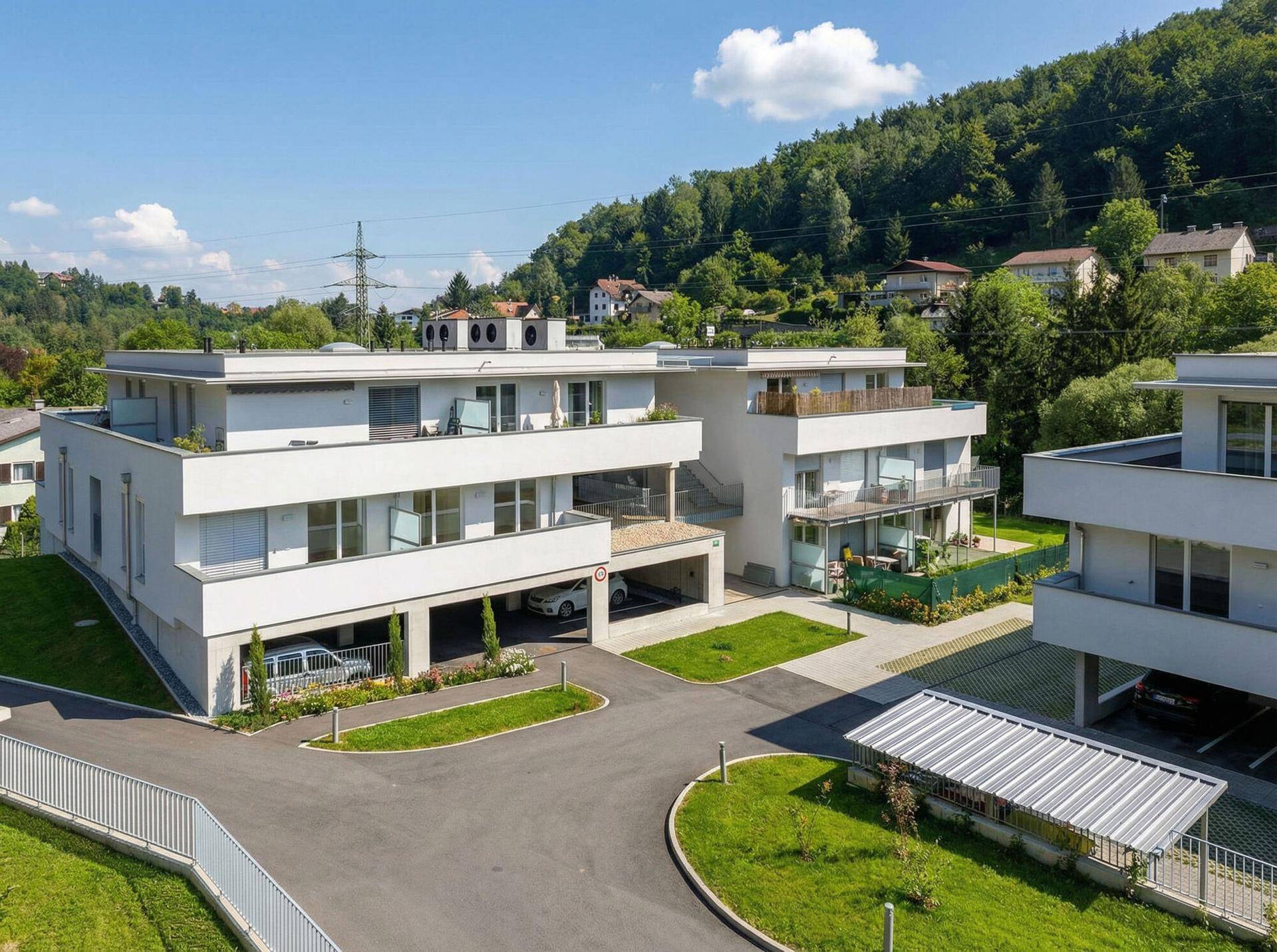 Moderne Wohnanlage mit mehreren Gebäuden, Tiefgarage und Carports in einer grünen Umgebung.