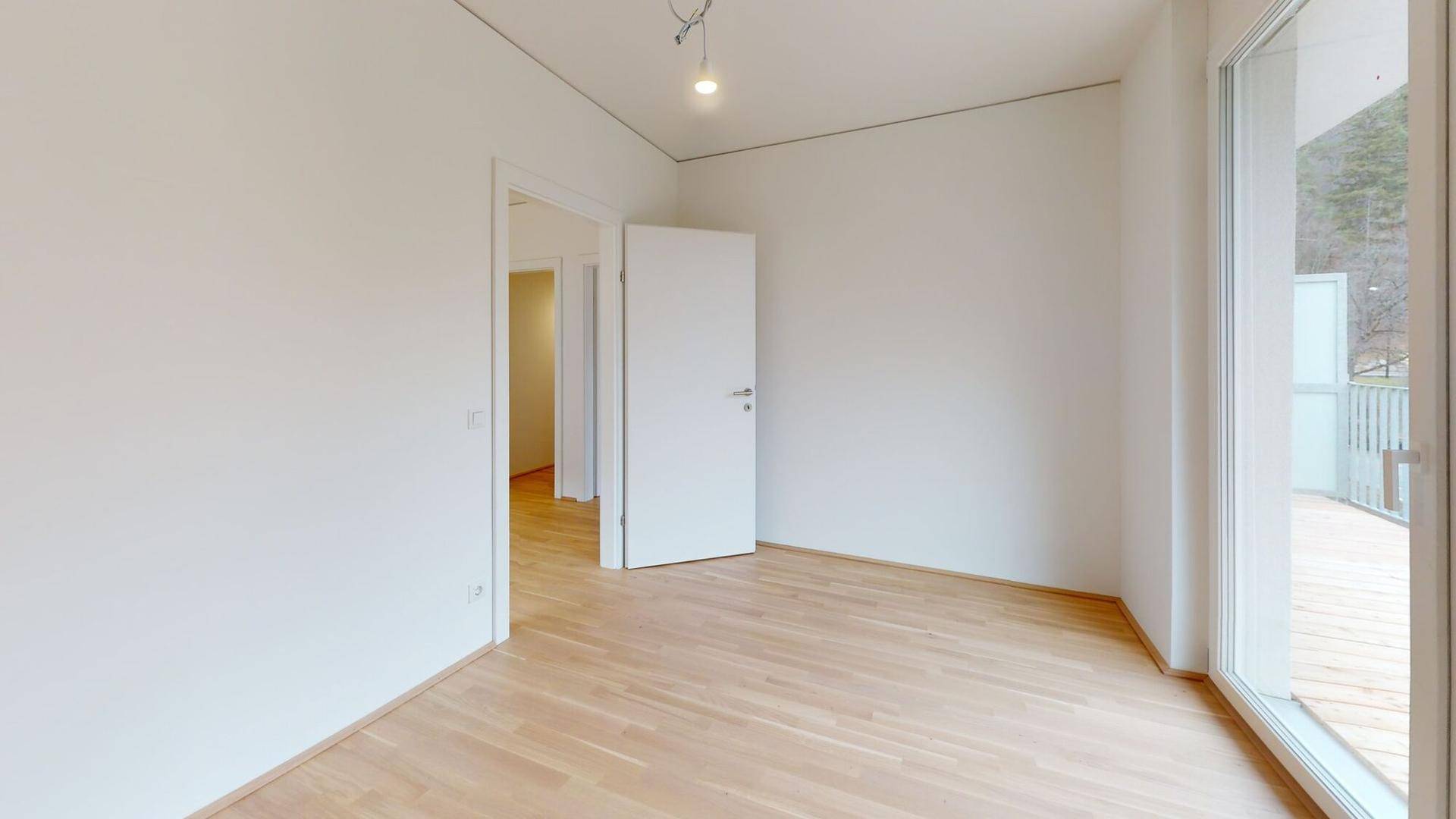 Helles Zimmer mit Holzboden und Zugang zu einem Balkon, bietet viel natürliches Licht.