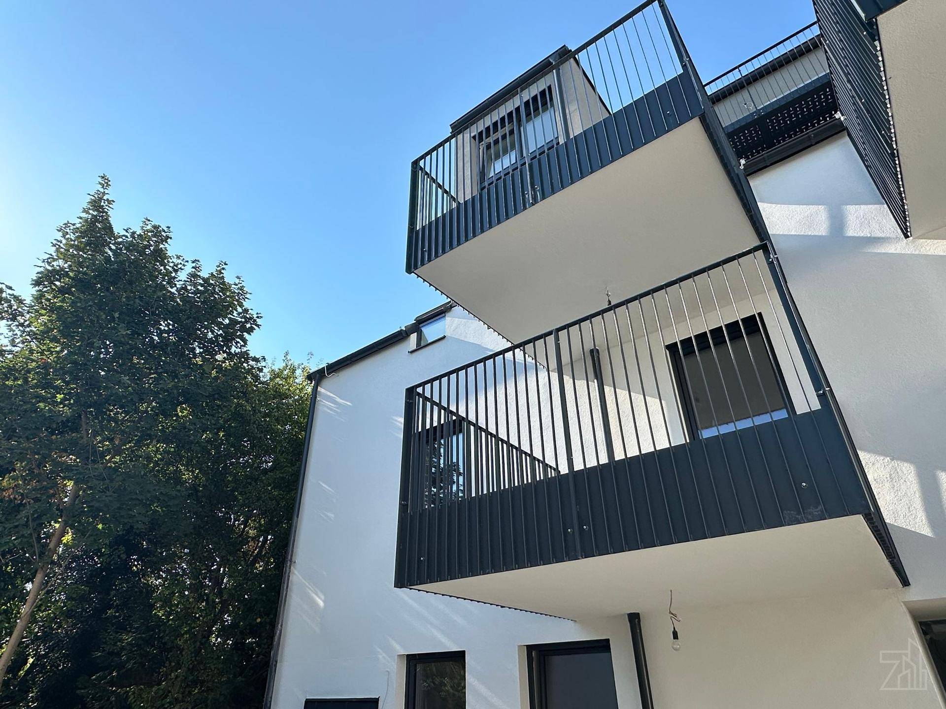 Moderne Gebäudefassade mit mehreren Balkonen und klaren Linien unter blauem Himmel.