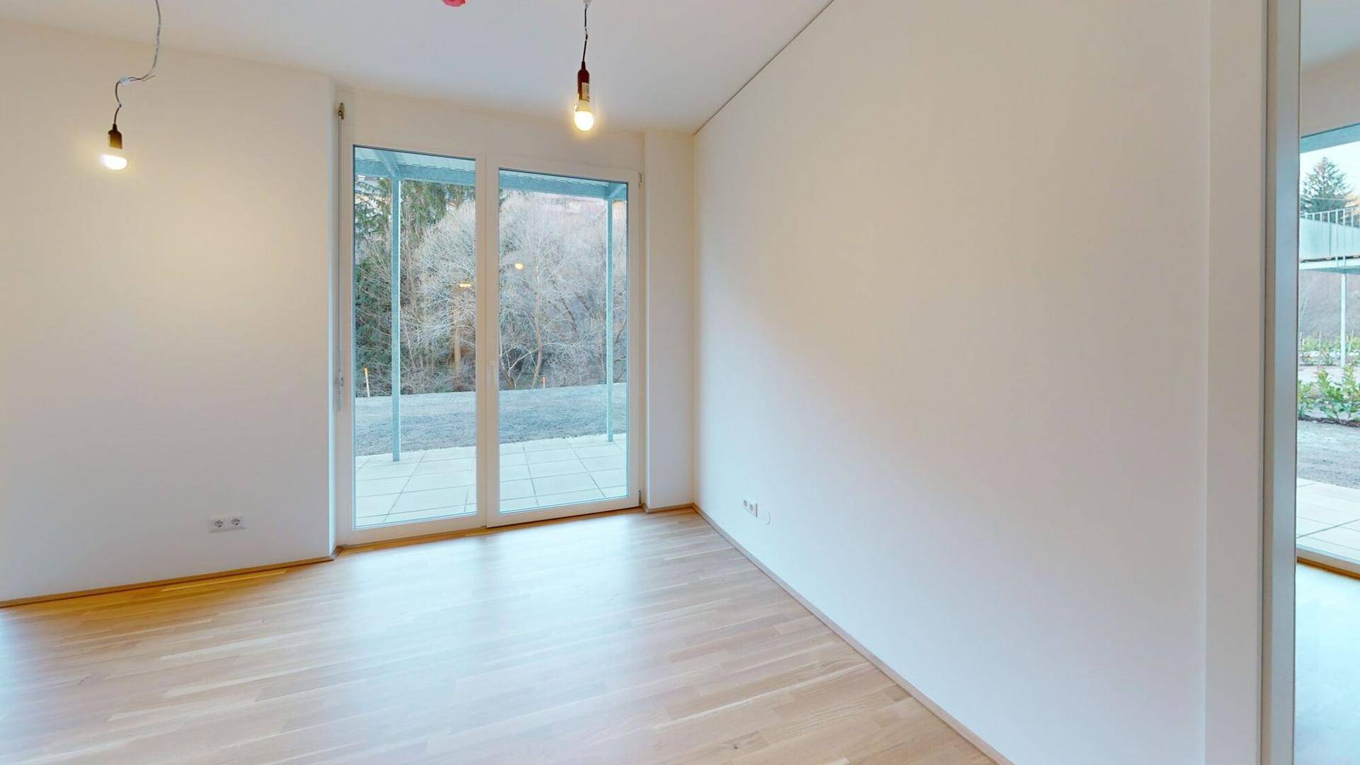 Heller, unmöblierter Raum mit Holzboden und Zugang zur Terrasse durch große Fenster.