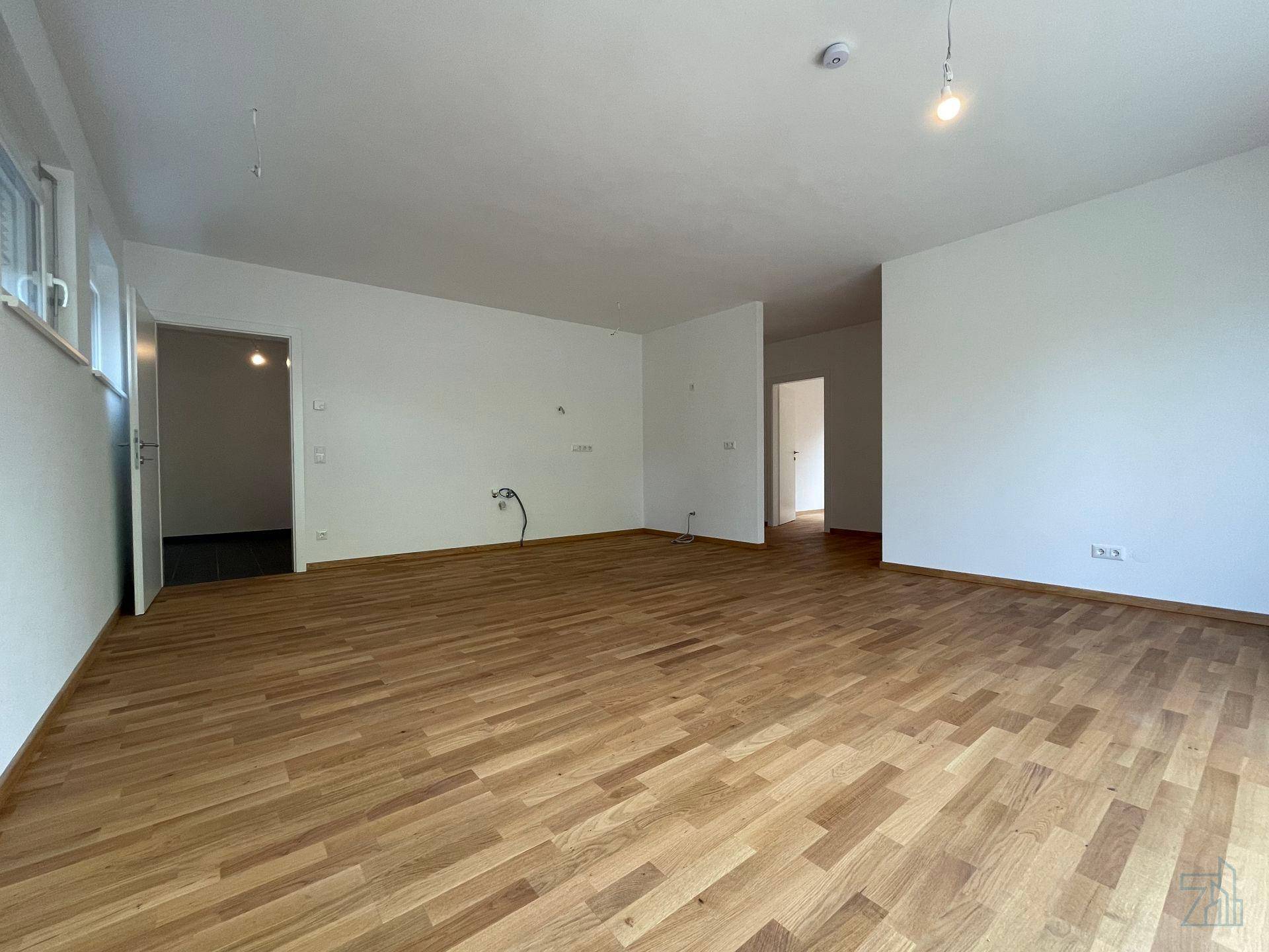Geräumiges, leeres Wohnzimmer mit Holzboden und offenen Durchgängen zu weiteren Räumen.