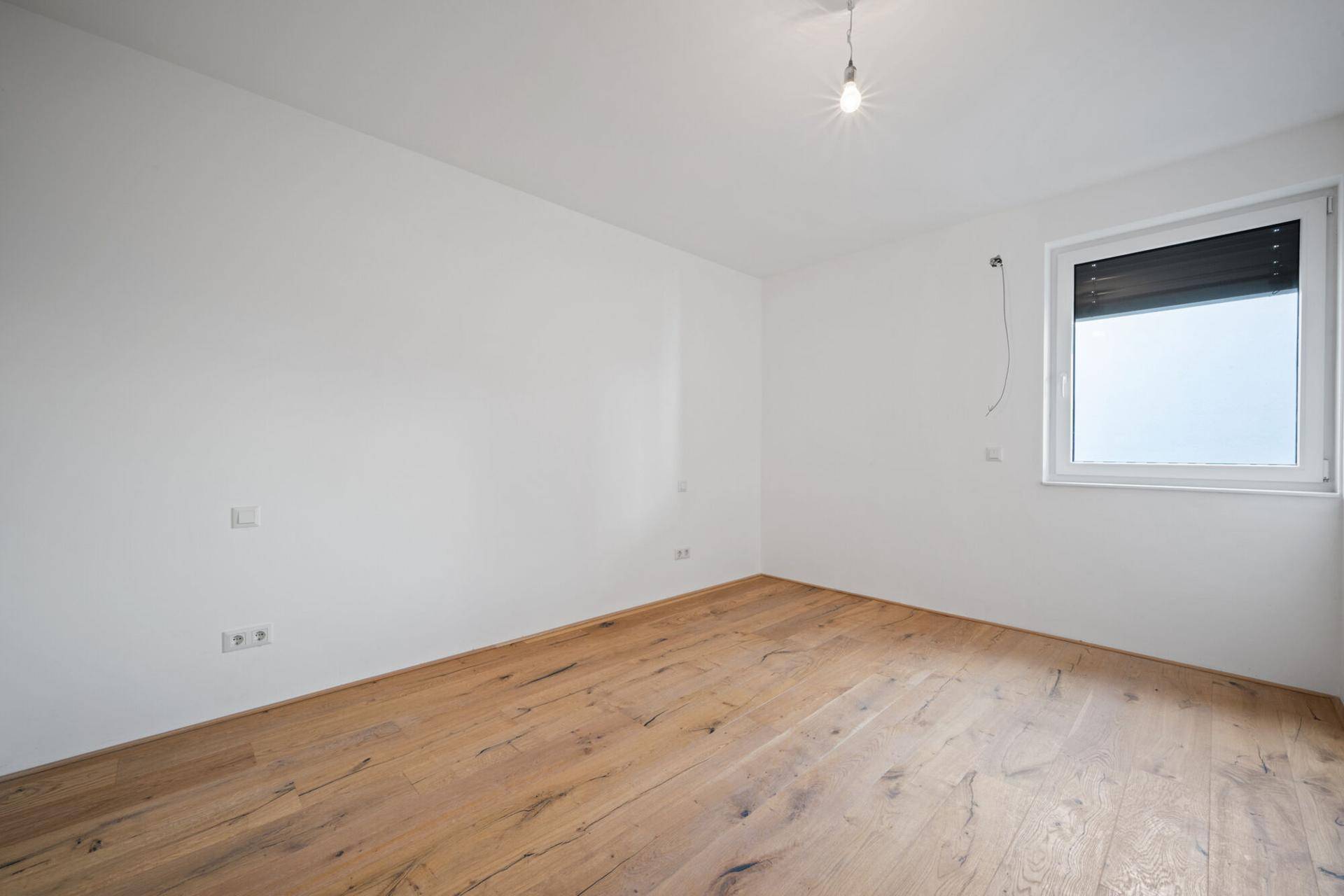 Helles, leeres Zimmer mit Holzdielenboden und einem Fenster, ideal als Schlaf- oder Arbeitszimmer.