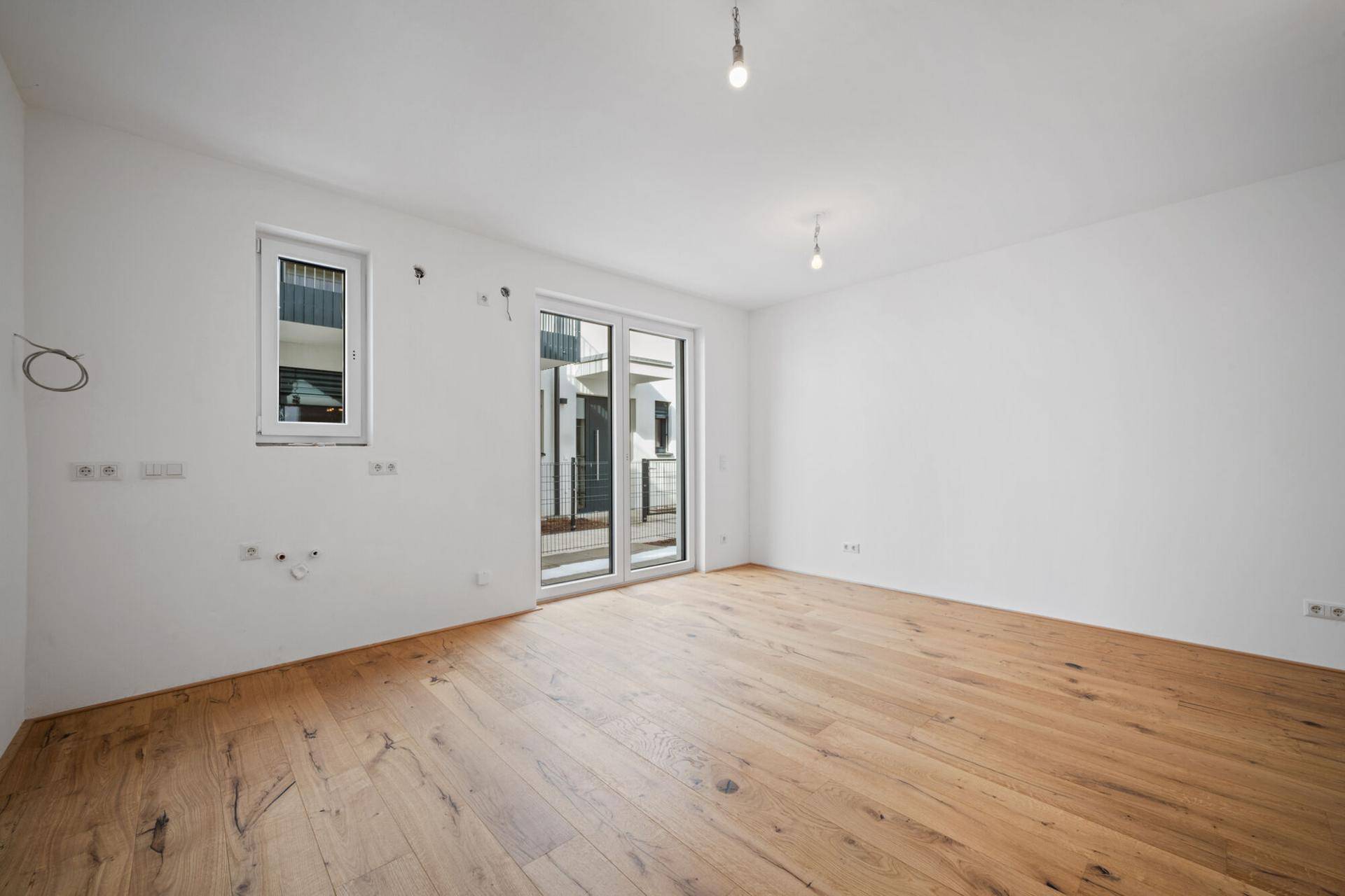 Geräumiges, unmöbliertes Zimmer mit Holzboden und Fenster zum Außenbereich.