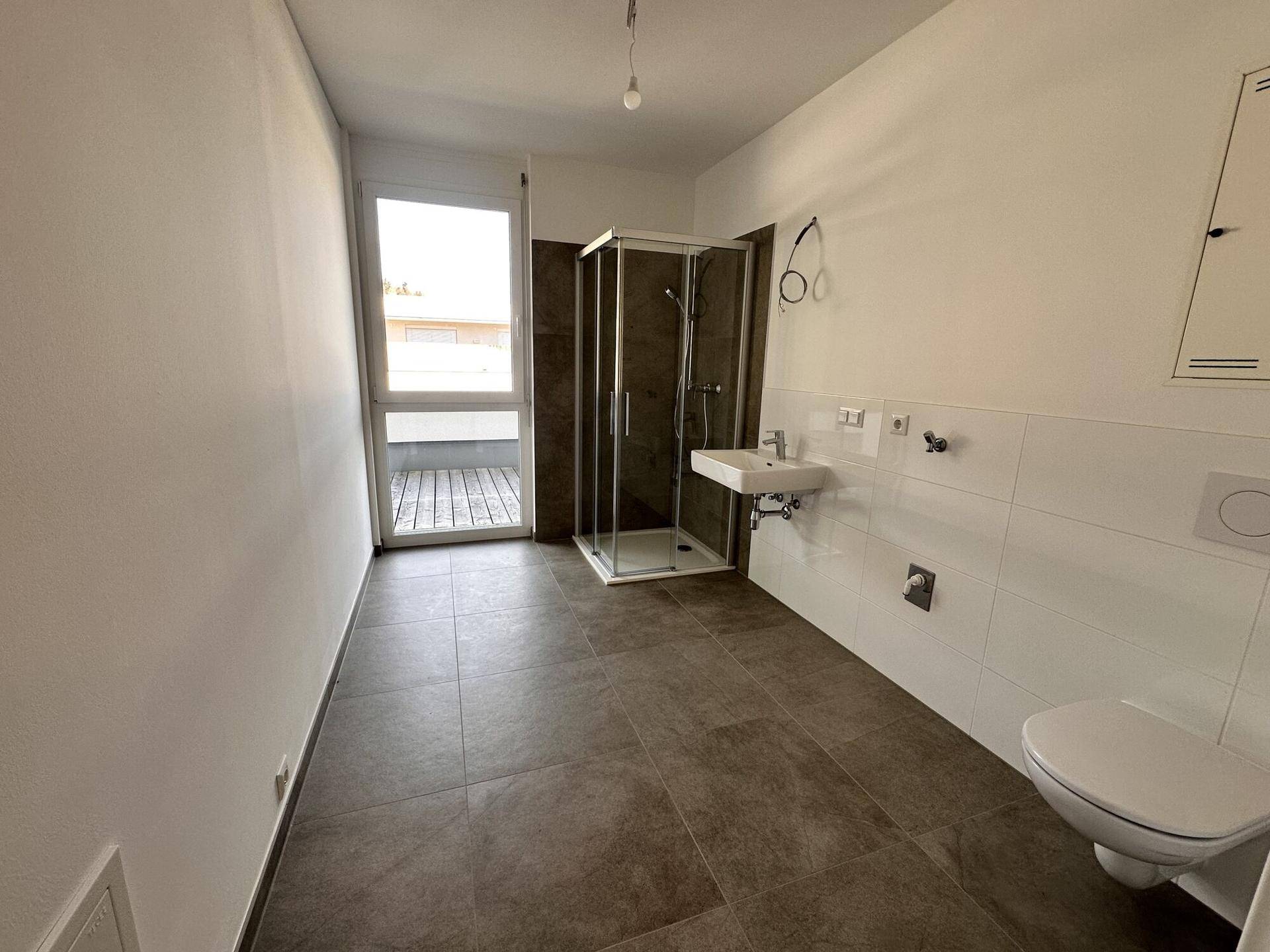 Helles Badezimmer mit Duschkabine, WC und Fliesenboden, bereit für die erste Nutzung.