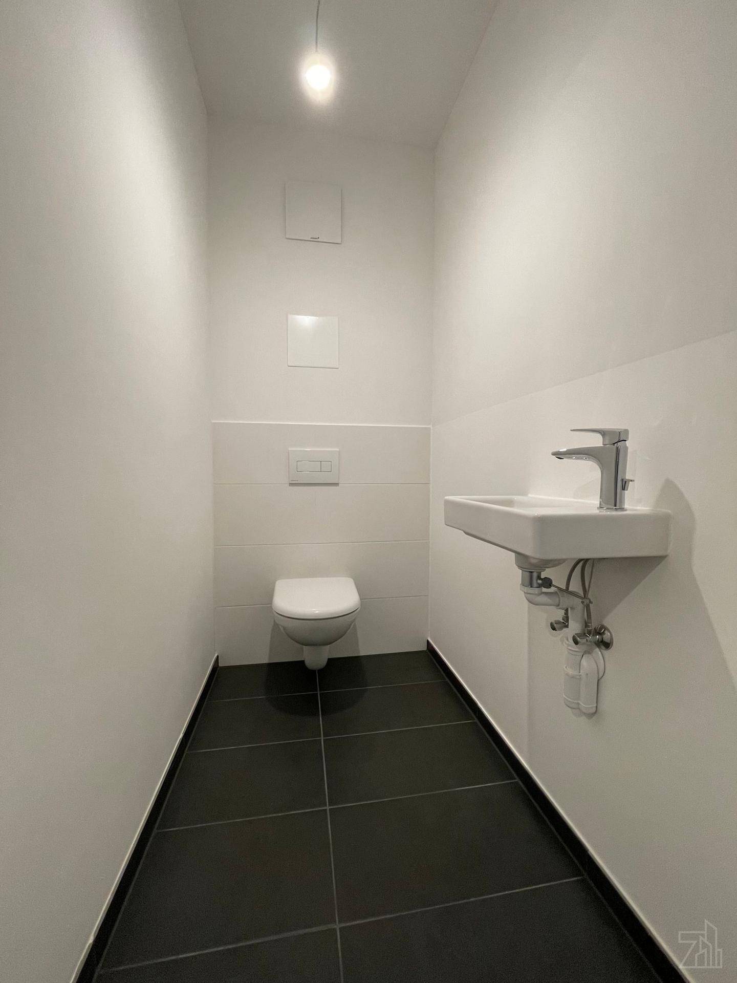 Kleines Gäste-WC mit wandhängendem WC, Waschbecken und dunklen Bodenfliesen.