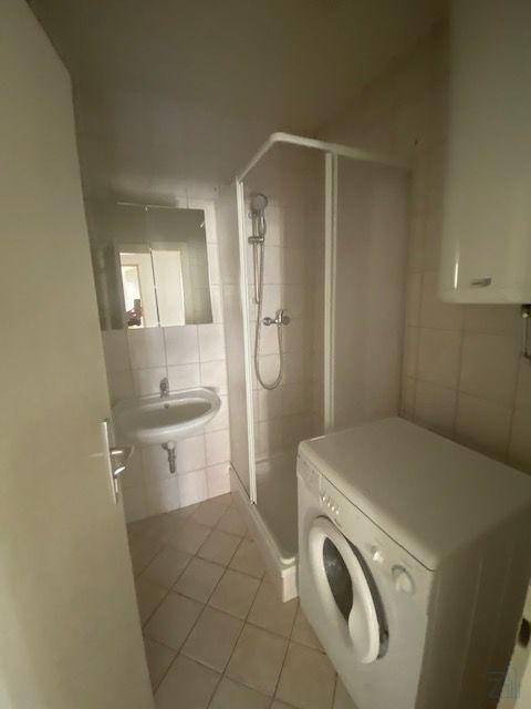 Funktionales Badezimmer mit Duschkabine, Waschbecken und Waschmaschine.