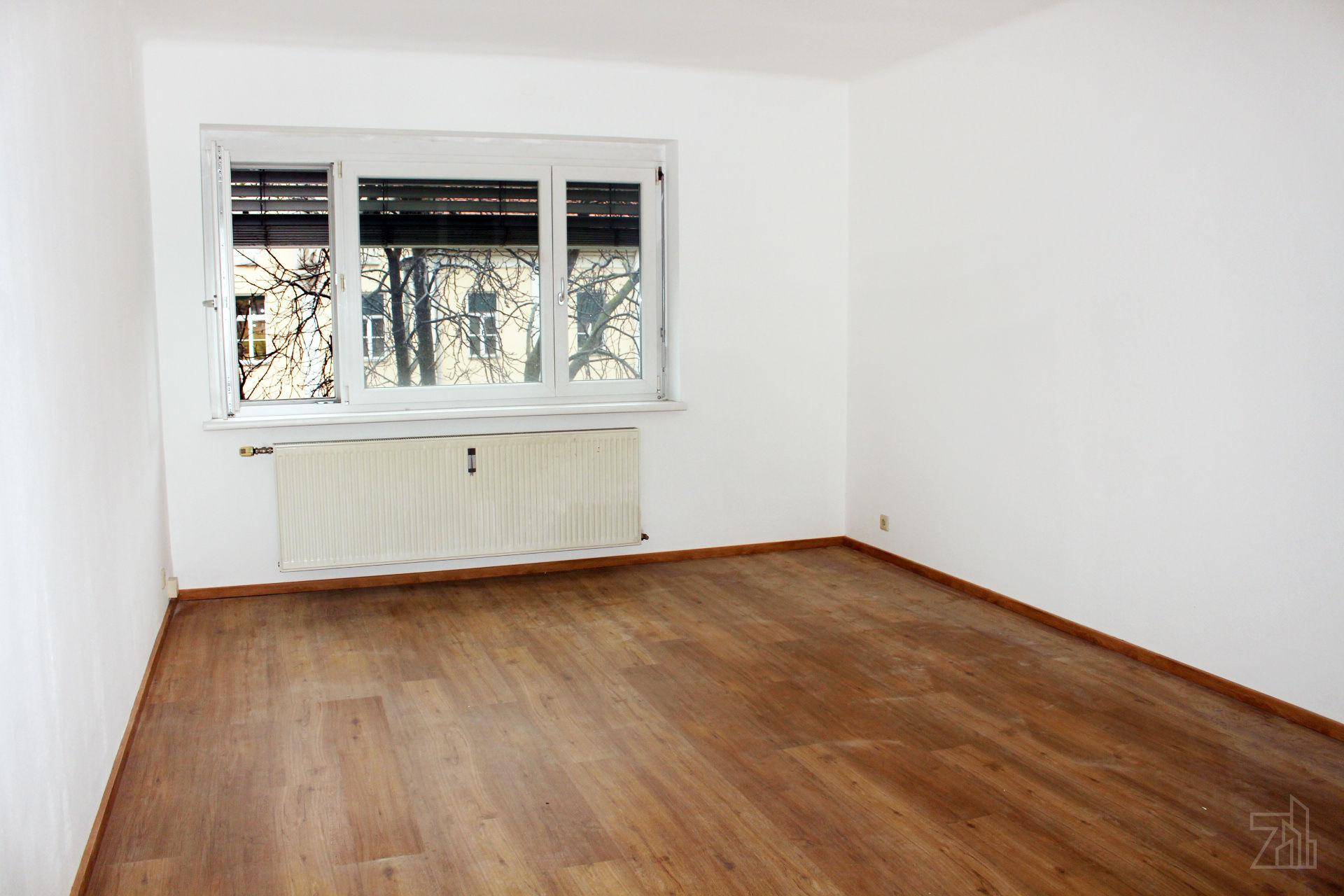 Heller Raum mit Laminatboden, weißen Wänden und großem Fenster mit Heizkörper.