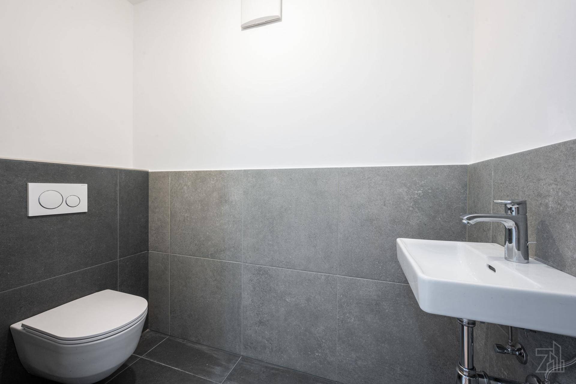 Modernes Gäste-WC mit wandhängender Toilette, kleinem Waschbecken und grauen Fliesen.