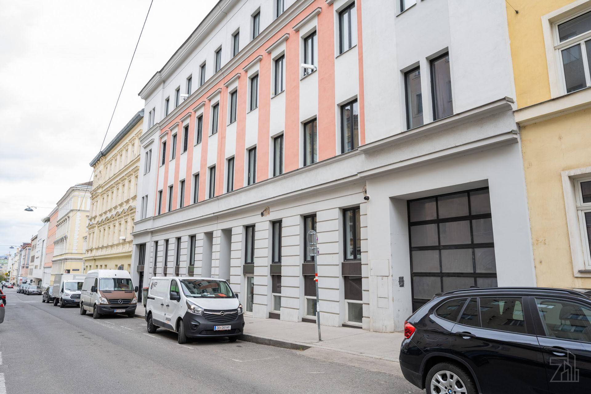 Seitenansicht des modernen Gebäudes an einer Stadtstraße mit parkenden Fahrzeugen.