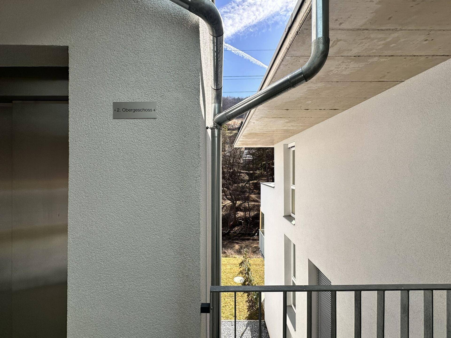 Moderner Eingangsbereich mit Aufzug und Hinweisschild zum Obergeschoss.