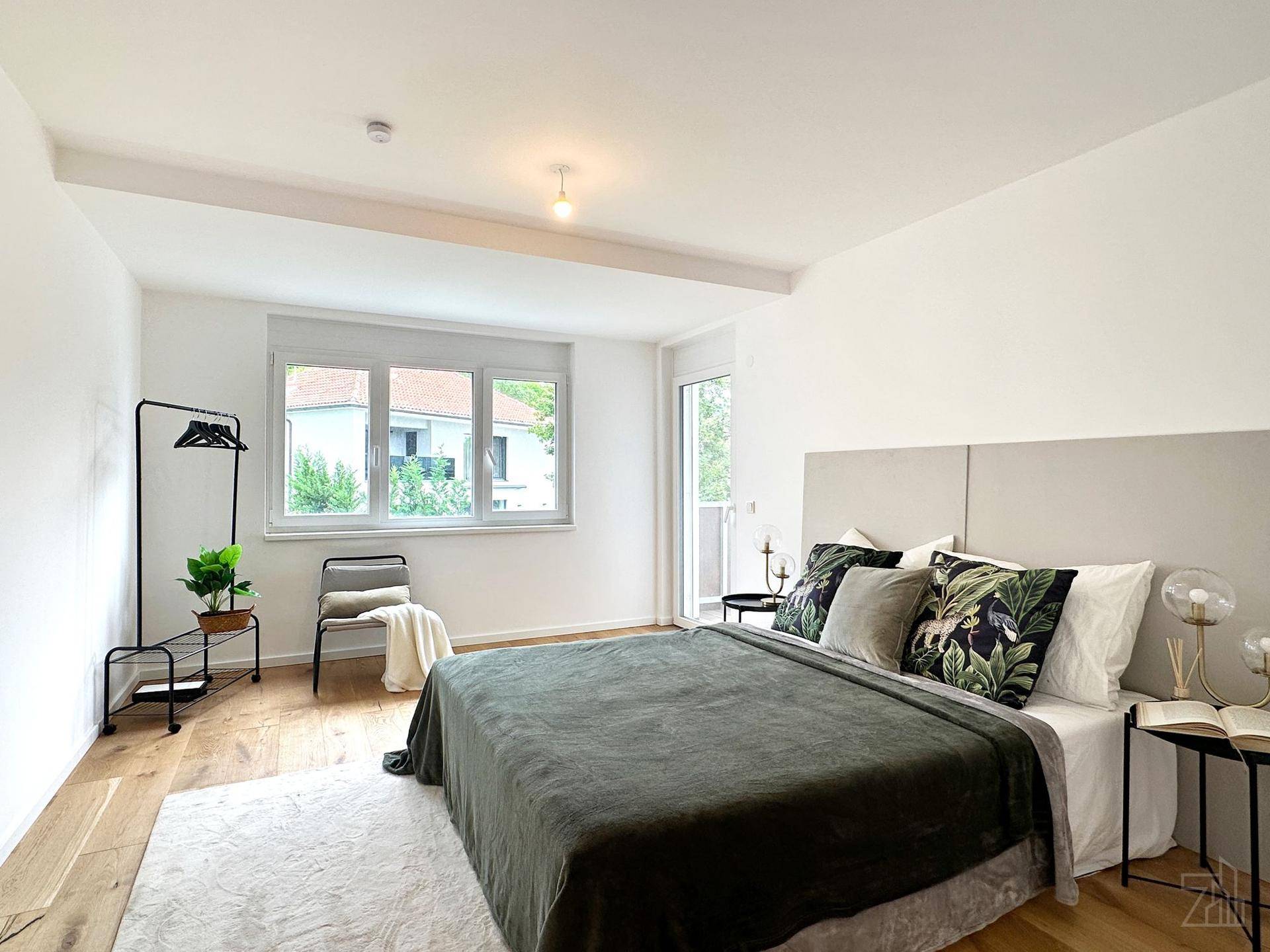 Geräumiges Schlafzimmer mit Holzboden, großem Bett und Zugang zu einem kleinen Balkon.