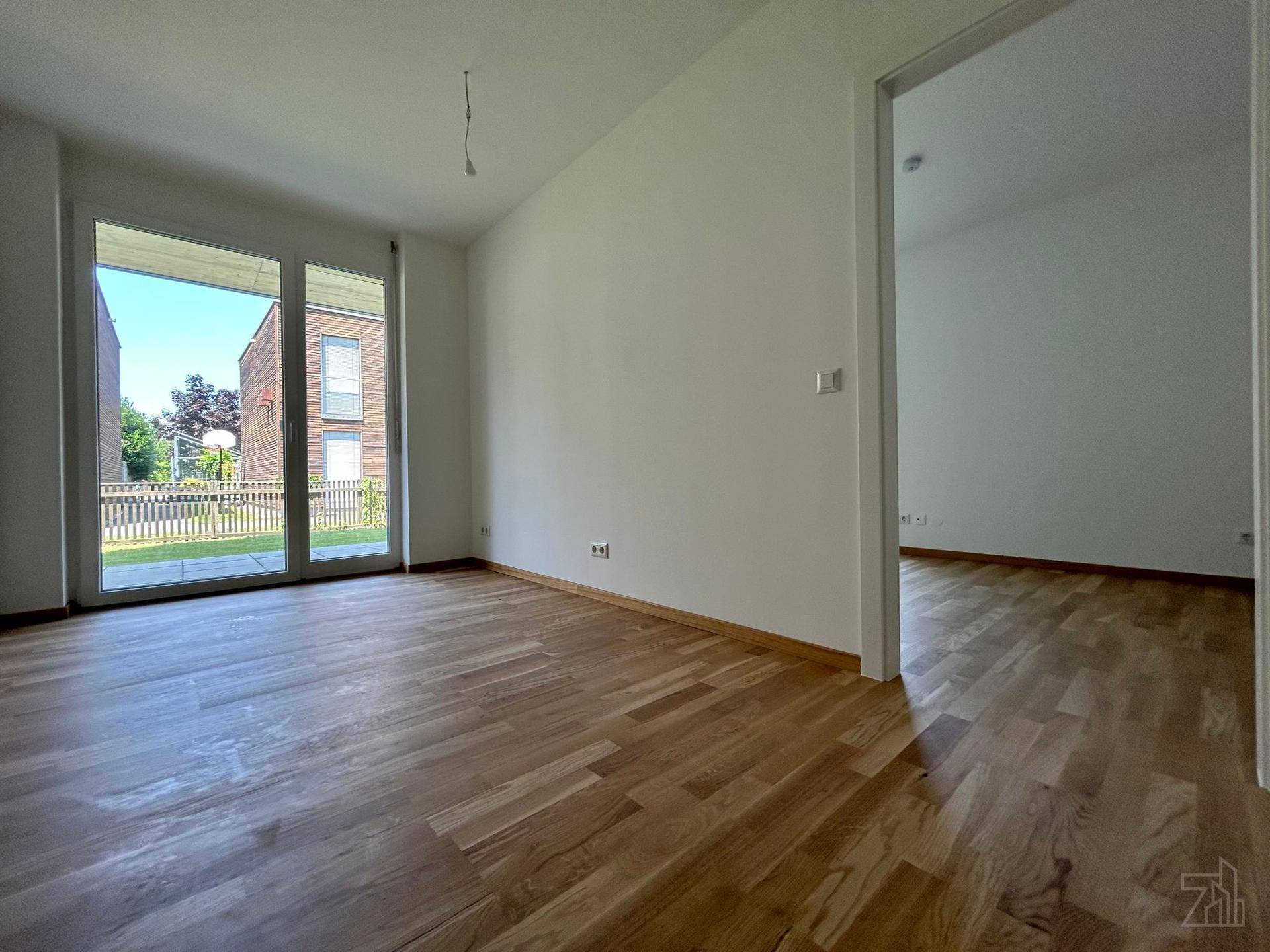 Geräumiger, heller Raum mit Parkettboden und großen Fenstertüren zum Gartenbereich.