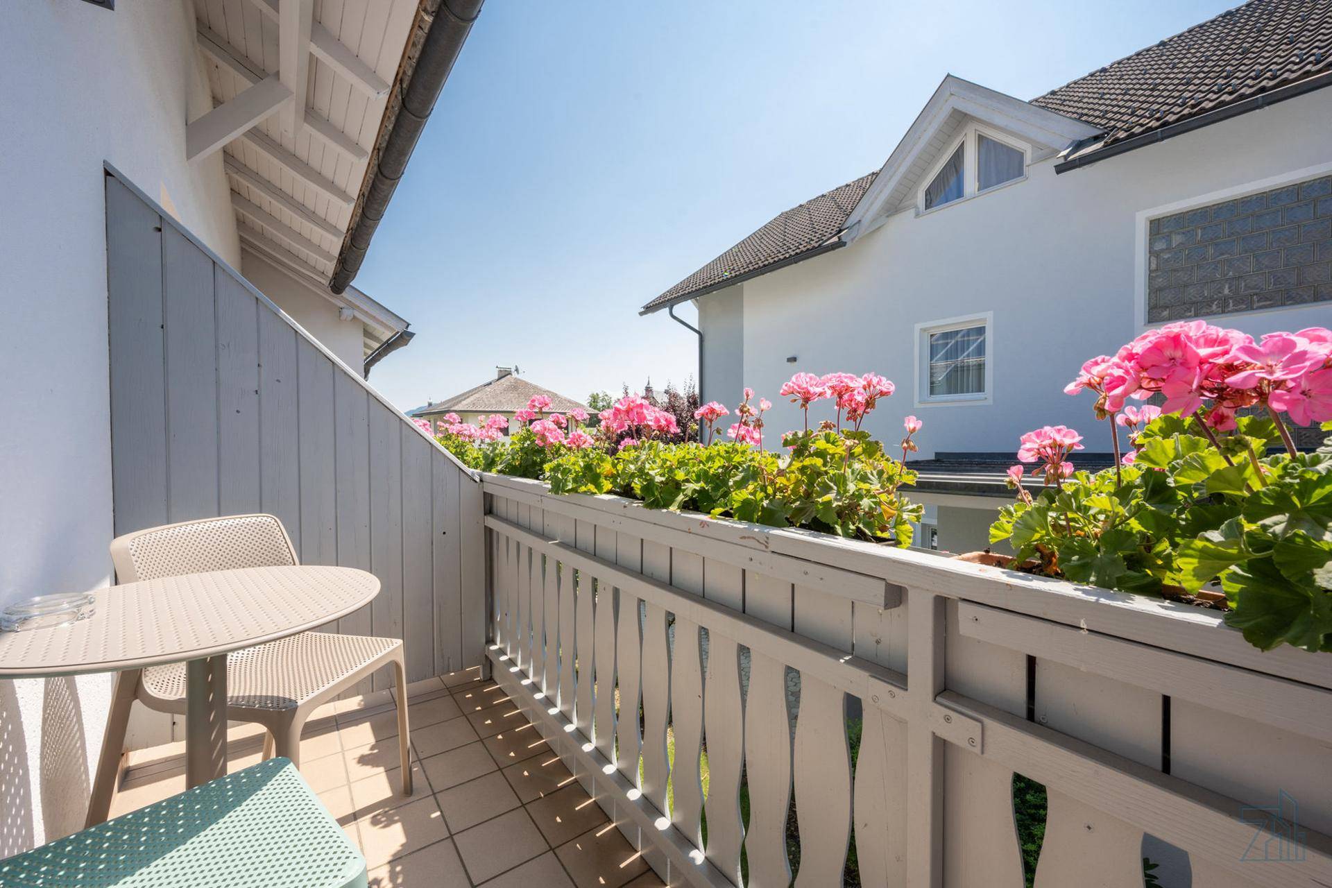 Balkon mit blühenden Geranien, Sitzgelegenheiten und Blick auf die Nachbarschaft.