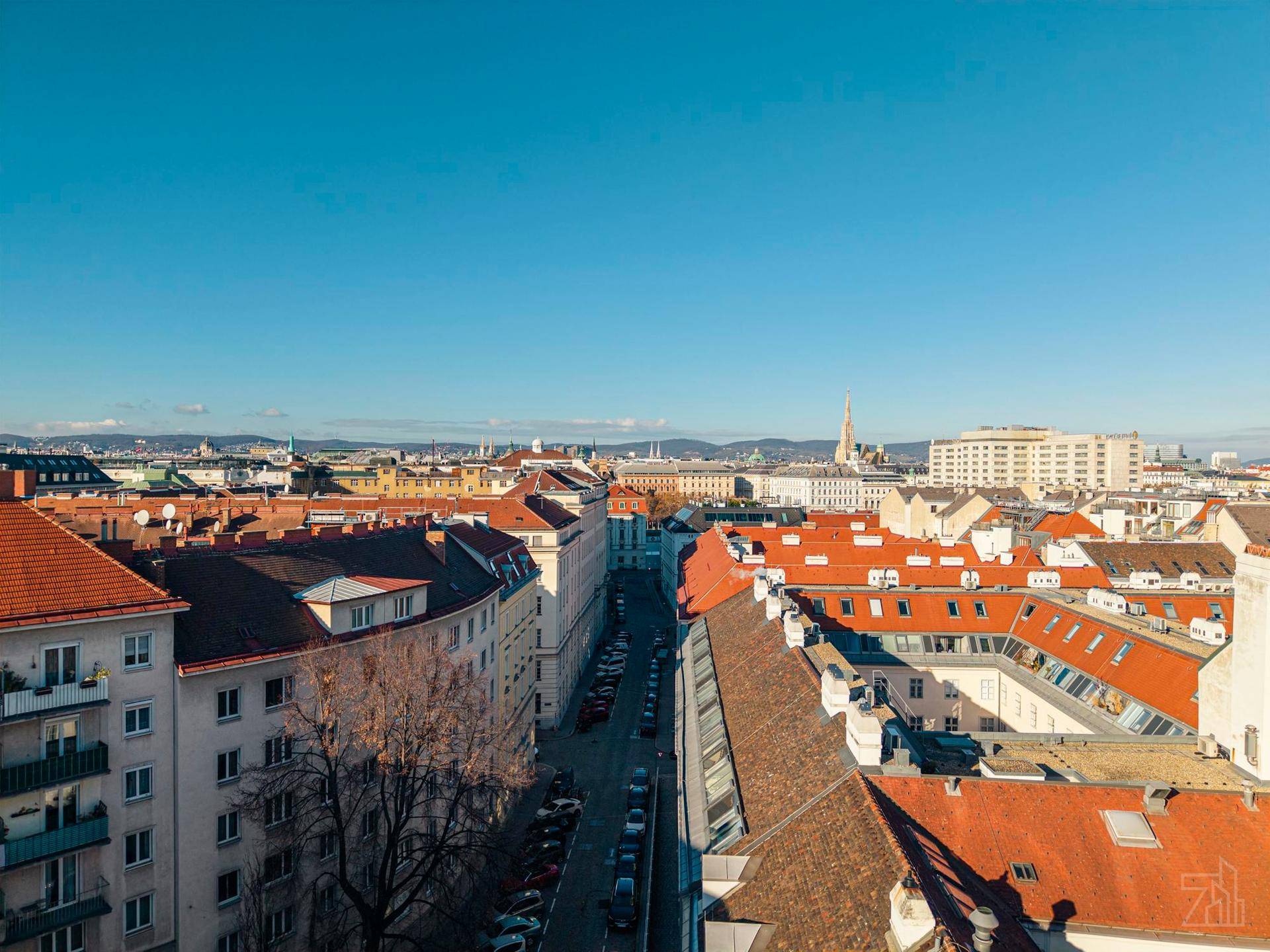 Weitläufiger Blick über die Dächer einer europäischen Stadt mit klarem blauem Himmel.
