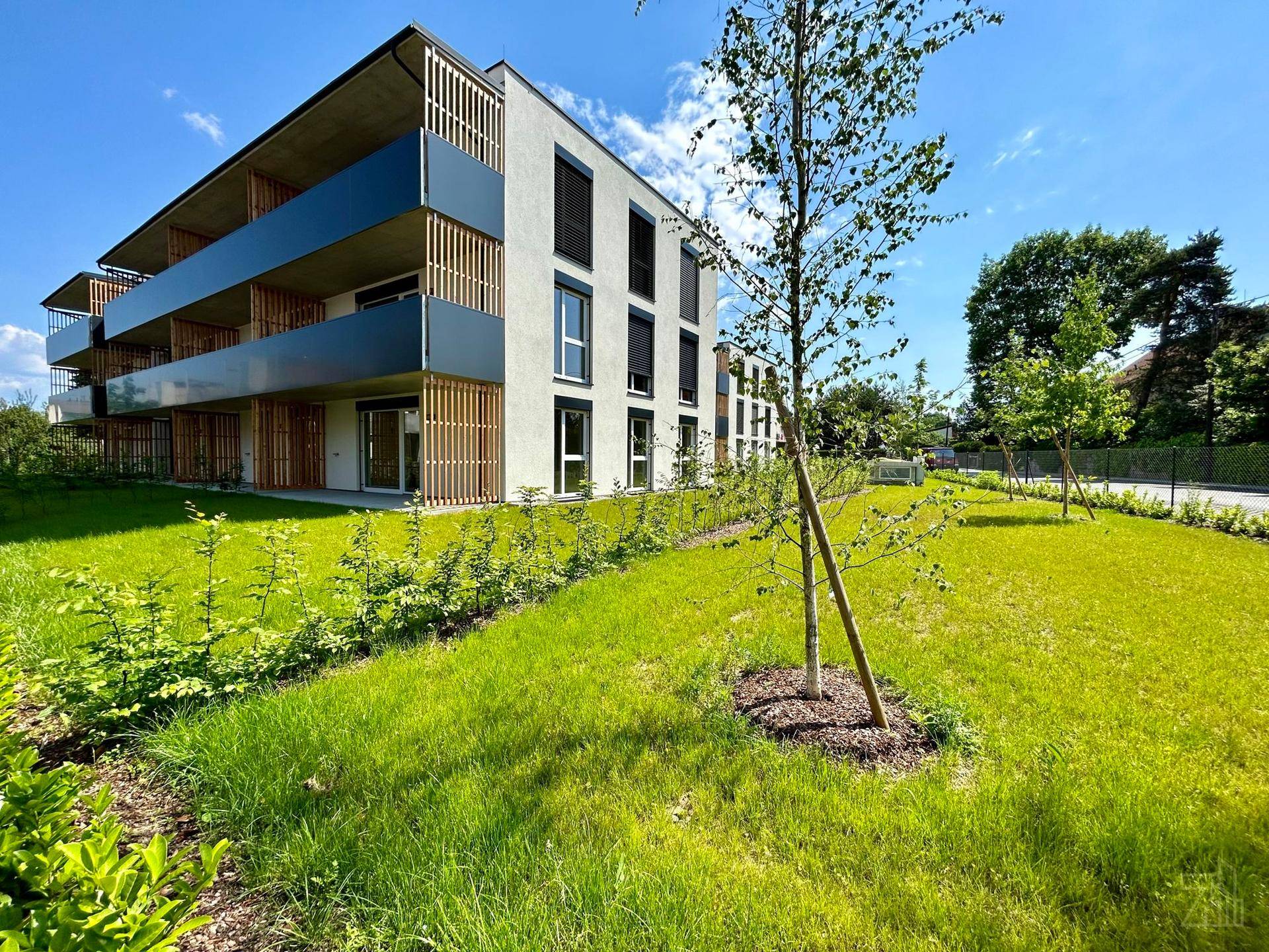 Neubau-Wohngebäude mit Balkonen und weitläufiger Grünfläche unter blauem Himmel.