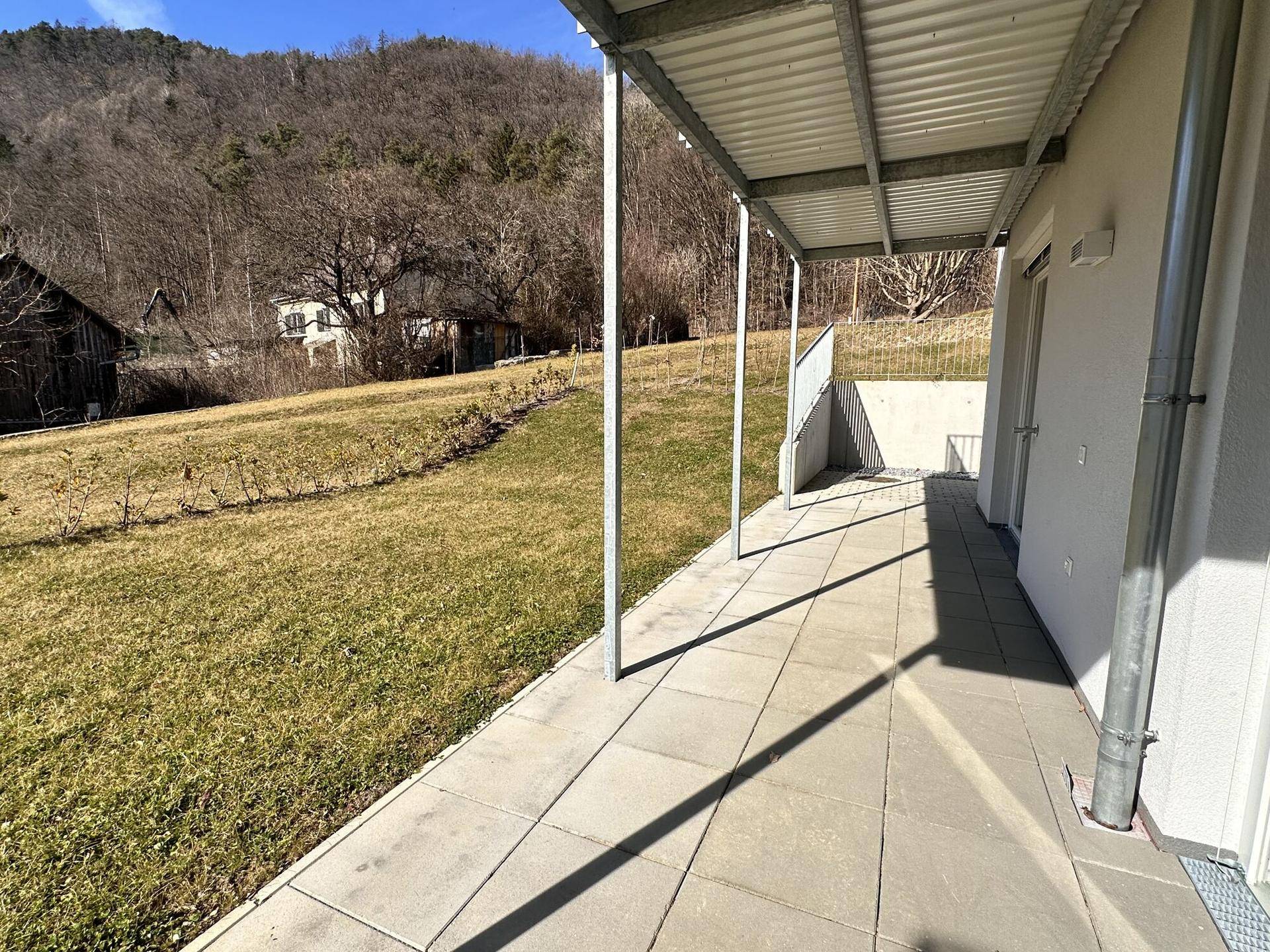 Überdachte Terrasse entlang der Hausseite mit Zugang zum Garten und Blick ins Grüne.
