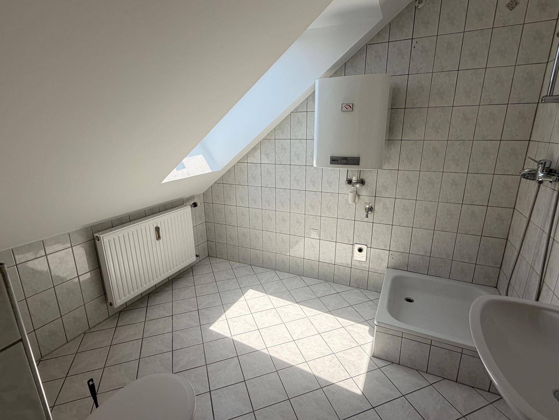 Gefliestes Badezimmer mit Dusche, Waschbecken und Dachschräge, gut beleuchtet durch ein Dachfenster.
