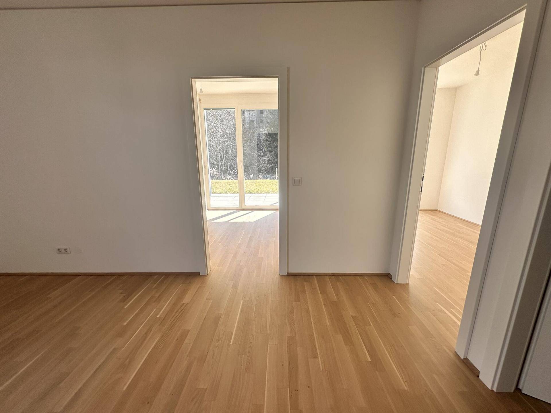 Heller, leerer Flur mit Holzparkettboden und Durchgängen zu angrenzenden Räumen mit viel Tageslicht.