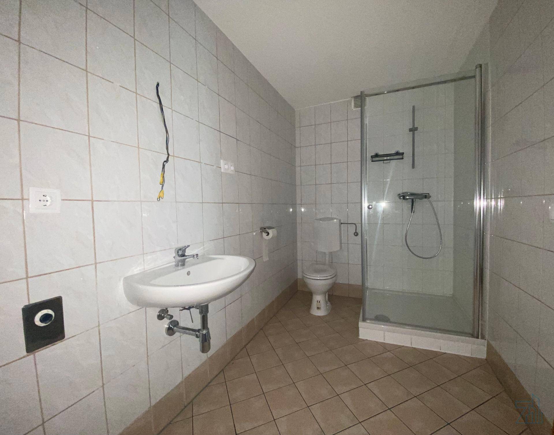 Badezimmer mit weißen Fliesen, Waschbecken, Toilette und einer Duschkabine.