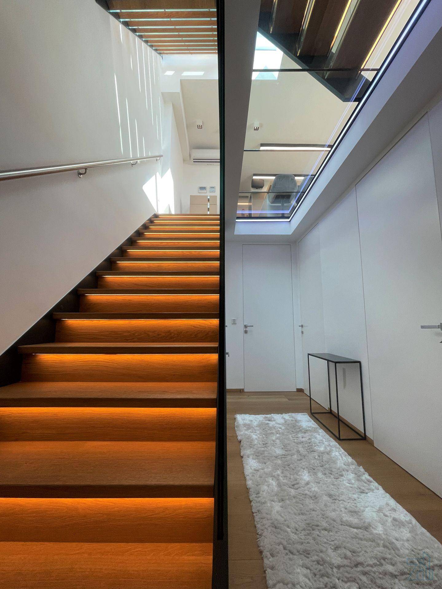 Elegante Holztreppe mit integrierter Beleuchtung und modernem Glasgeländer in hellem Ambiente.