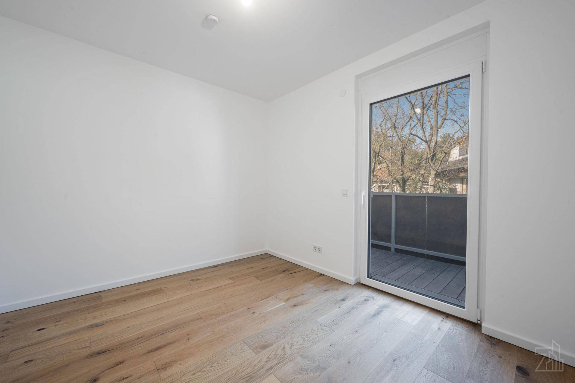 Heller, leerer Raum mit Holzboden und Schiebetür, die zu einem kleinen Balkon führt.