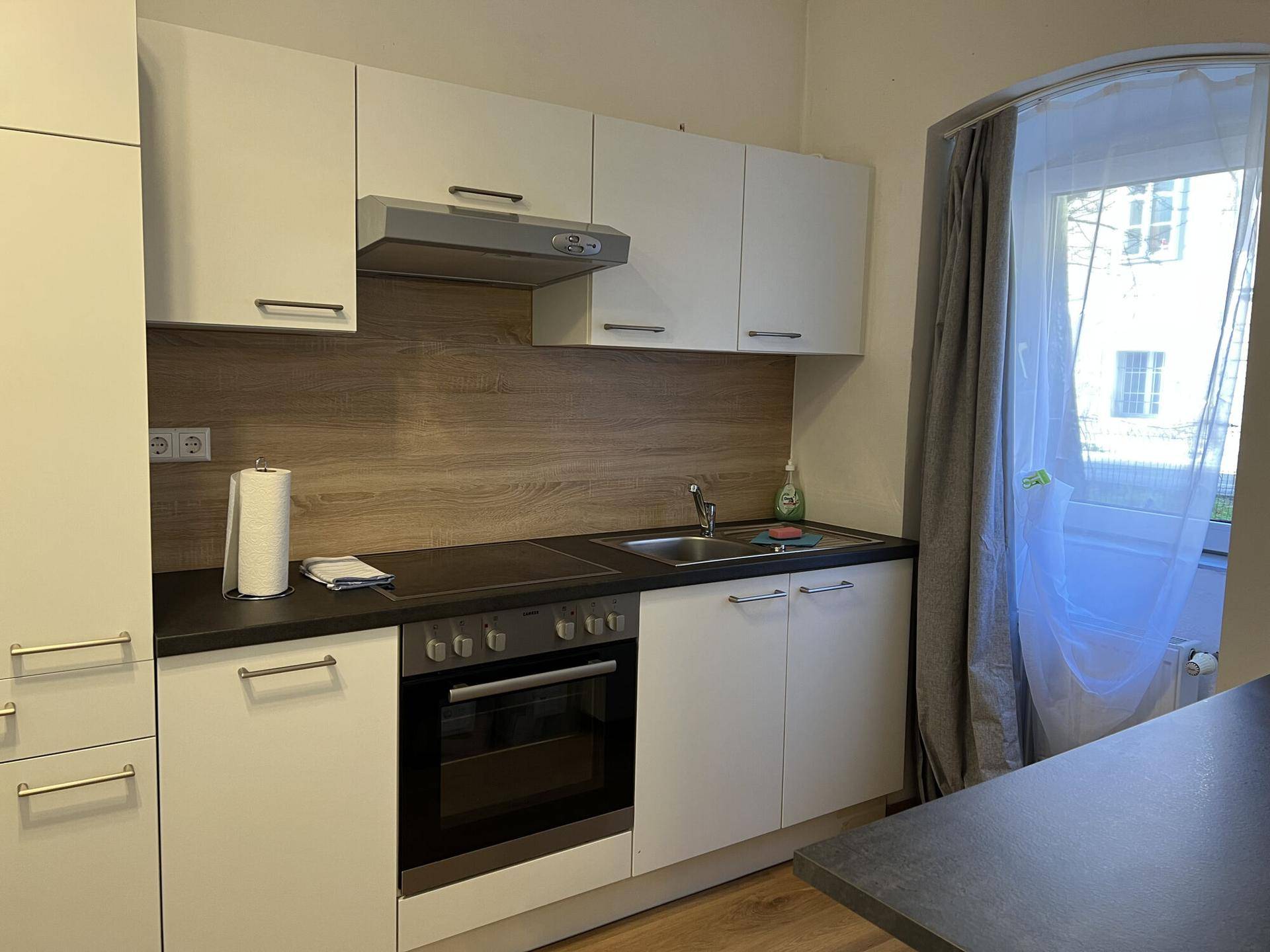 Kleine Küchenzeile mit weißen Schränken, Backofen und Fenster.