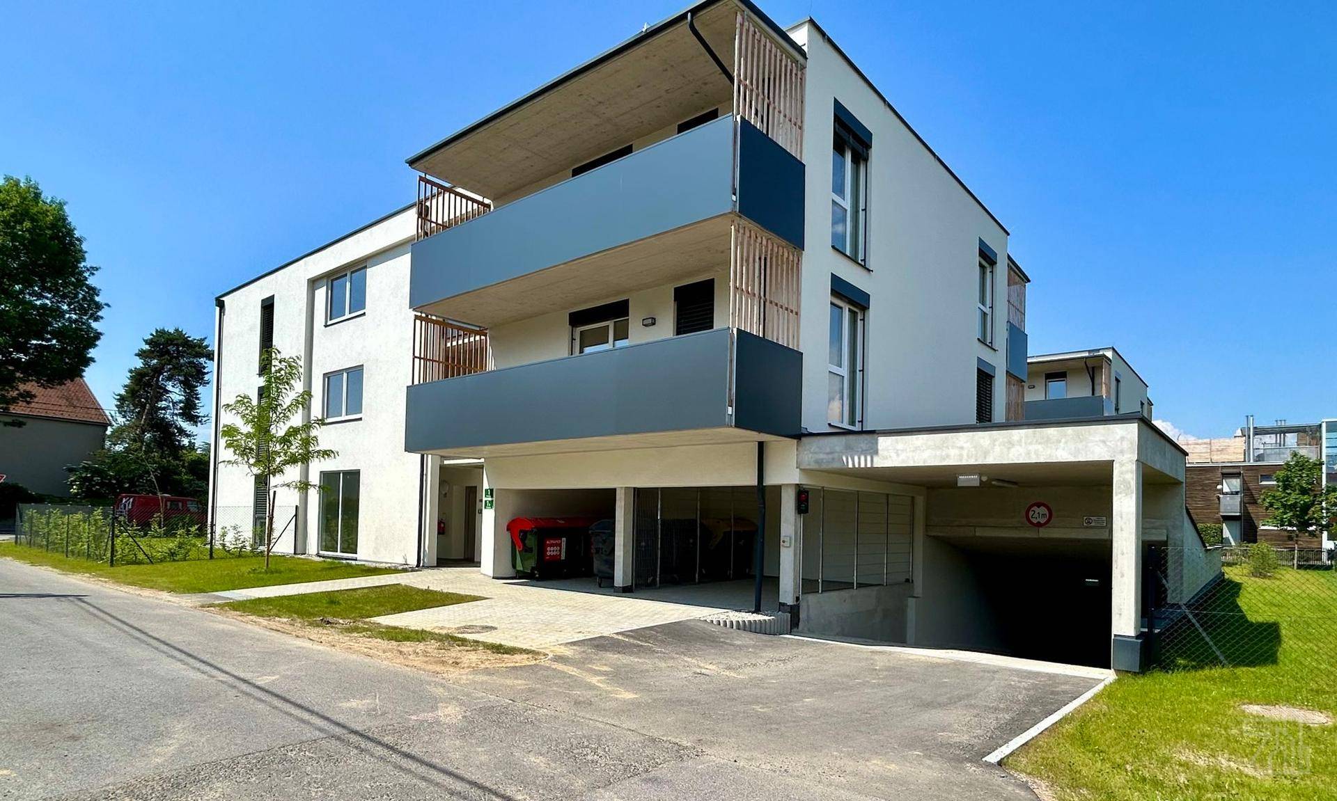 Modernes Apartmentgebäude von der Straße aus gesehen mit Balkonen und Zufahrt zur Tiefgarage.