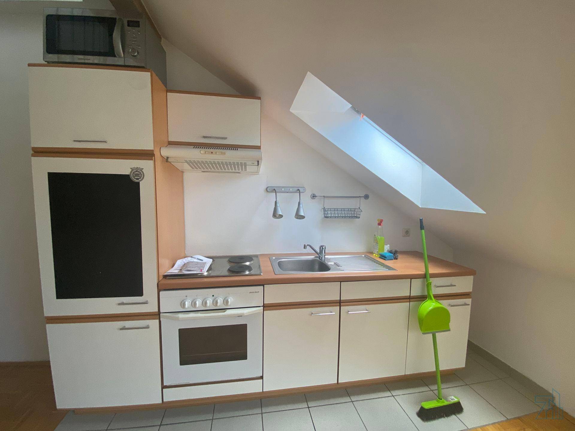 Kompakte Küchenzeile mit Herd, Spüle und Mikrowelle unter einem Dachfenster, praktisch und funktional.