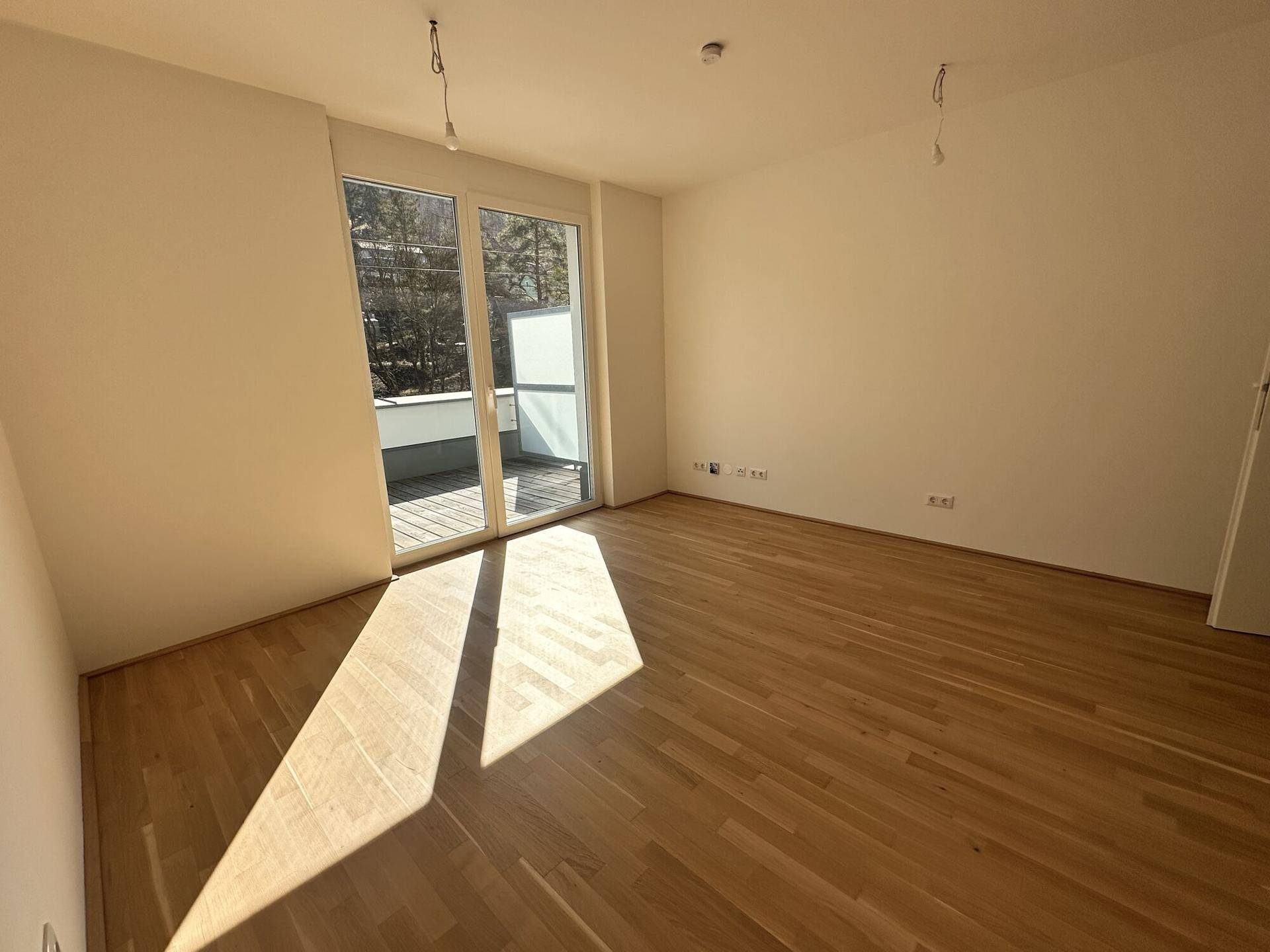 Geräumiges Zimmer mit hellem Parkettboden und direktem Zugang zur sonnigen Außenterrasse.
