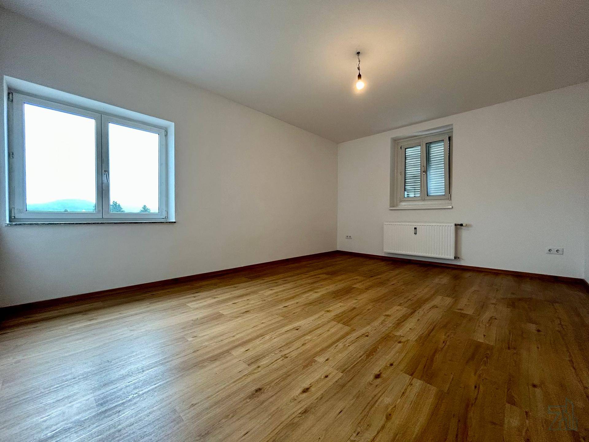Geräumiger Raum mit zwei Fenstern, Laminatboden und weißen Wänden, ideal als Schlafzimmer.