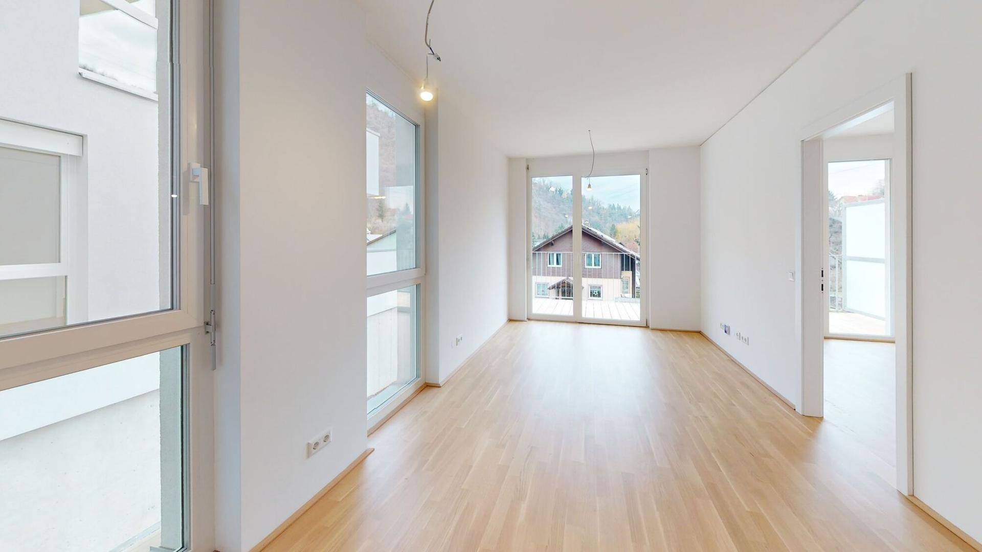 Helles Wohnzimmer mit Parkettboden, großen Fenstern und Zugang zum Balkon.