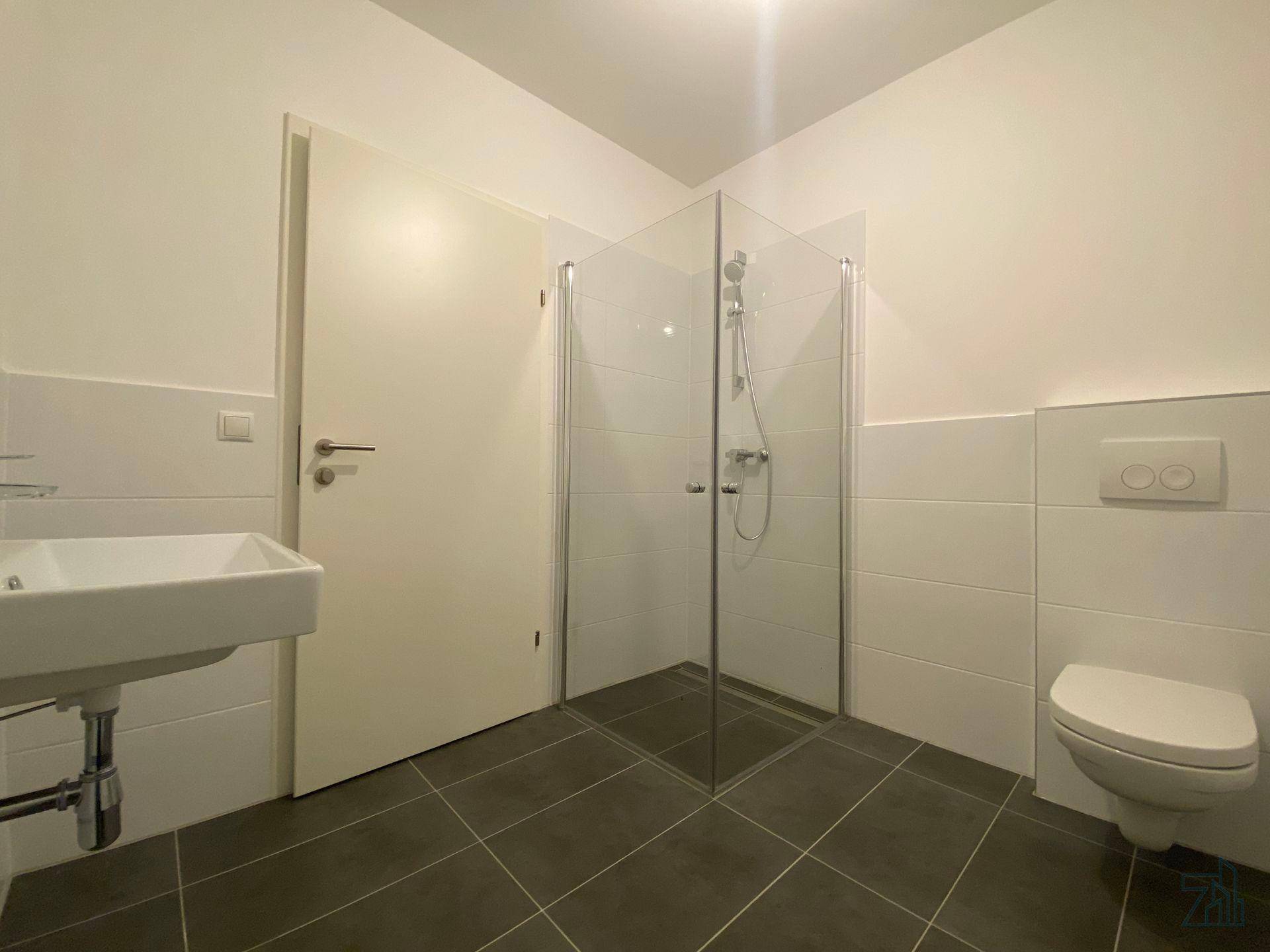Modernes Badezimmer mit Duschkabine, Waschbecken und Toilette auf dunklen Fliesen.