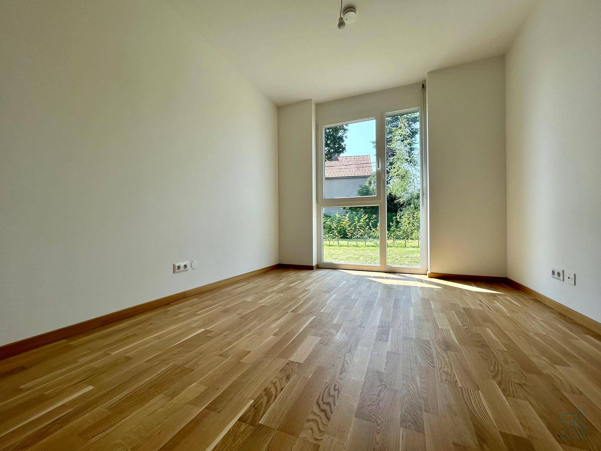 Geräumiges Schlafzimmer mit hellem Parkettboden und großen Fenstern mit Blick ins Grüne.