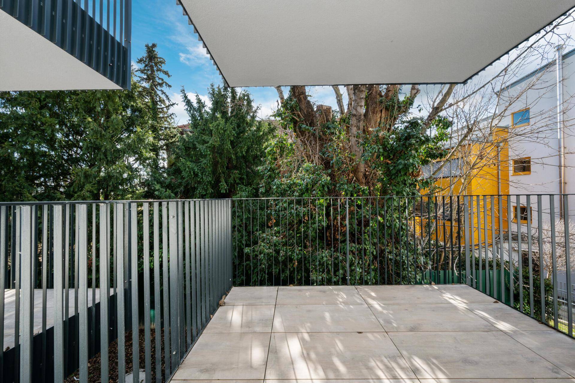 Balkon mit Fliesenboden und einem ruhigen Blick ins Grüne mit alten Bäumen.