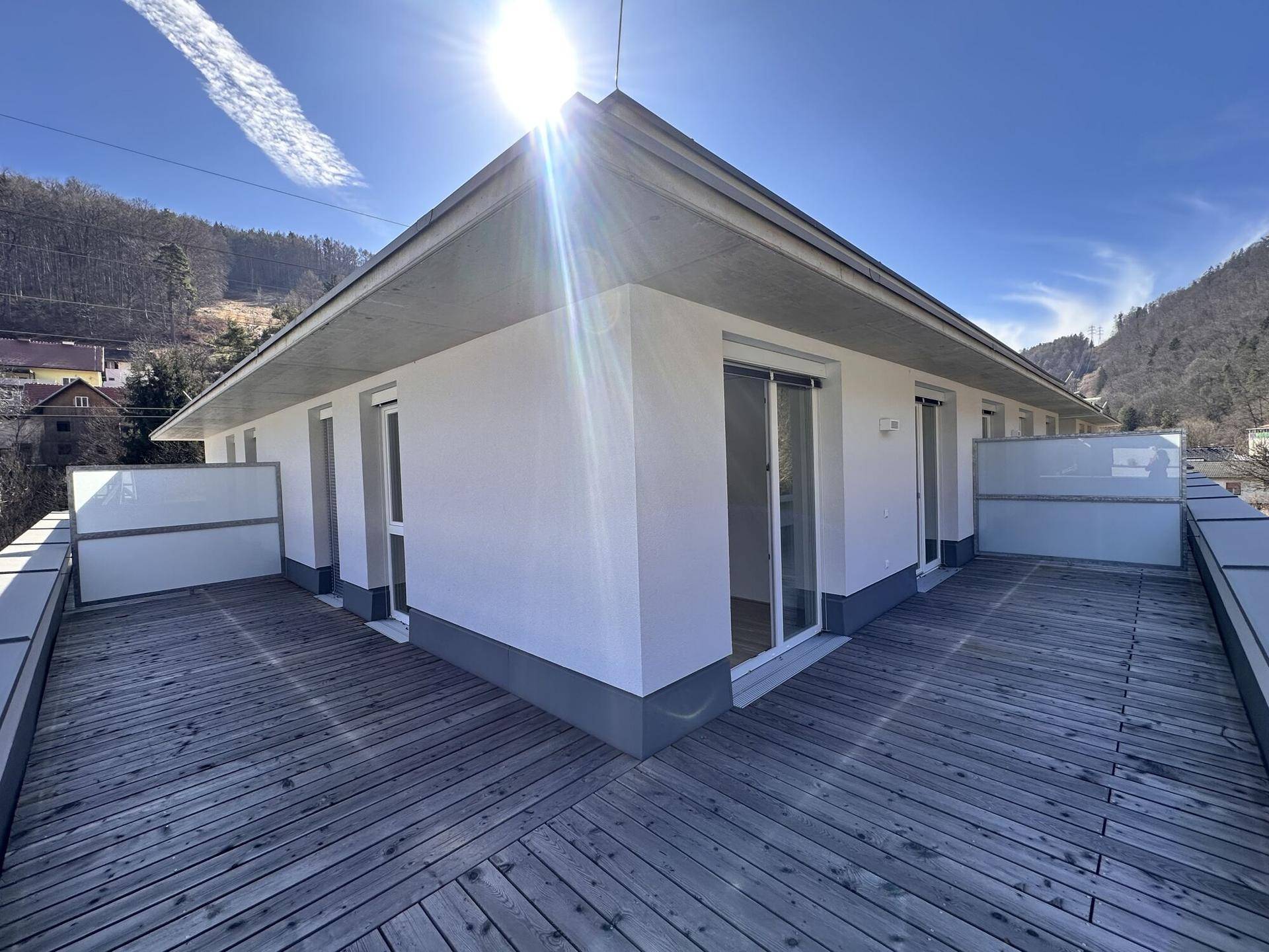 Sonnige Dachterrasse mit Holzboden und moderner Architektur, umgeben von Natur.