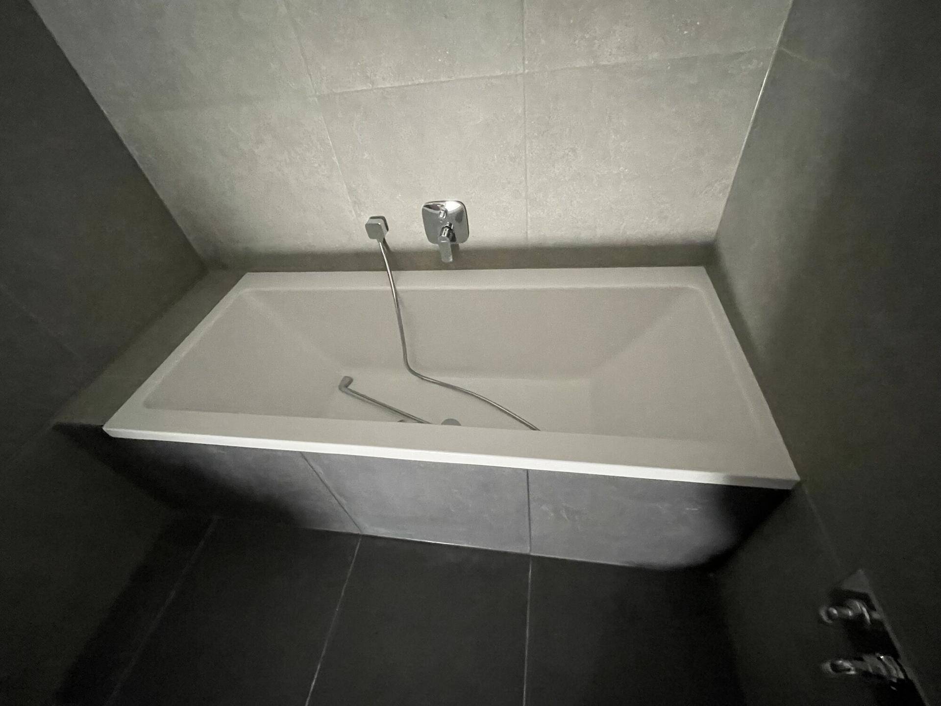 Nahaufnahme einer modernen, eingebauten Badewanne mit Armaturen in einem gefliesten Badezimmer.
